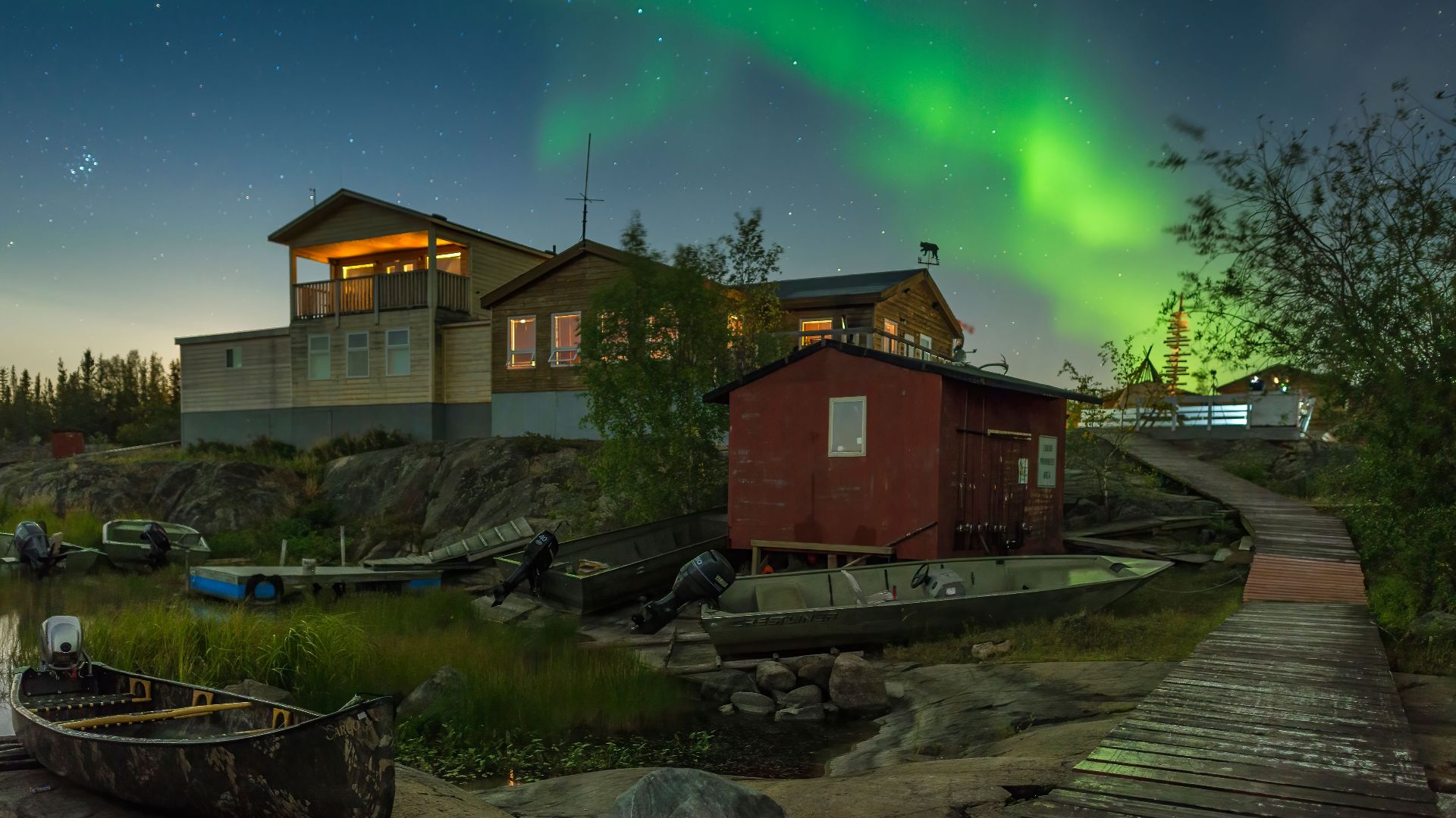 Colorful aurora borealis over rustic lakeside cabins and boats in Yellowknife, Canada.