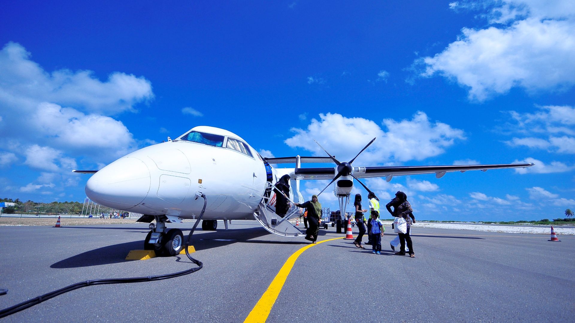 A group of people board a propeller airplane on a sunny day in Fuvahmulah, Maldives.
