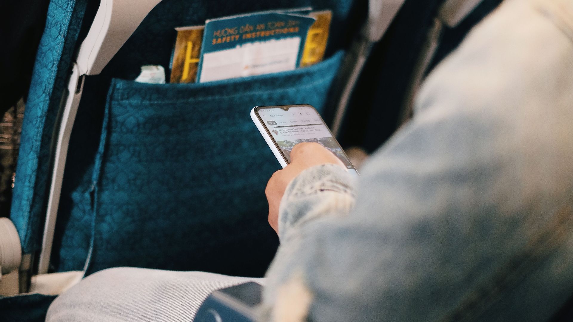 Passenger using smartphone while seated on airplane for entertainment or work.