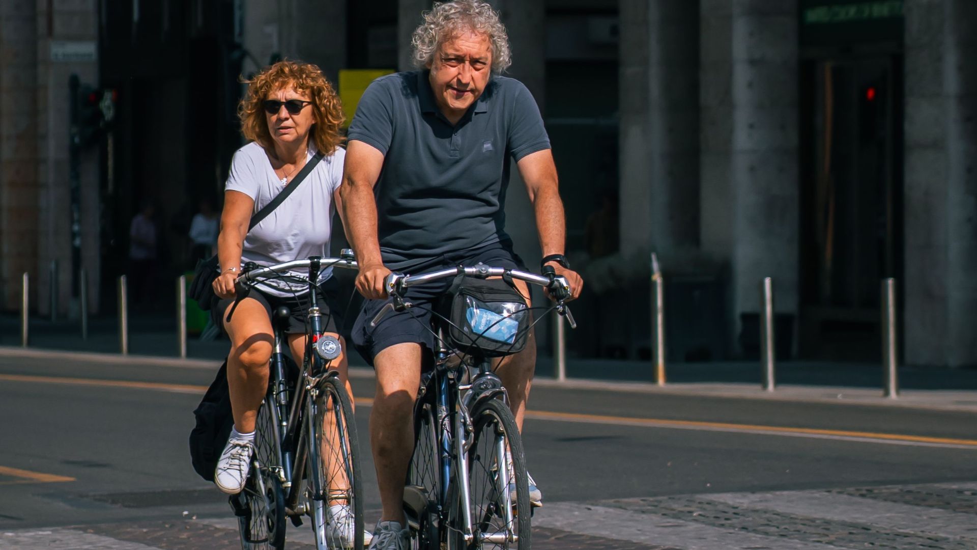 A senior couple enjoying a leisurely bicycle ride through a sunny city street, promoting active lifestyle.