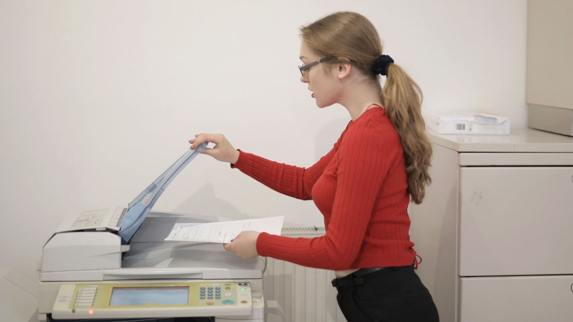 An office employee using a photocopier to copy documents indoors.