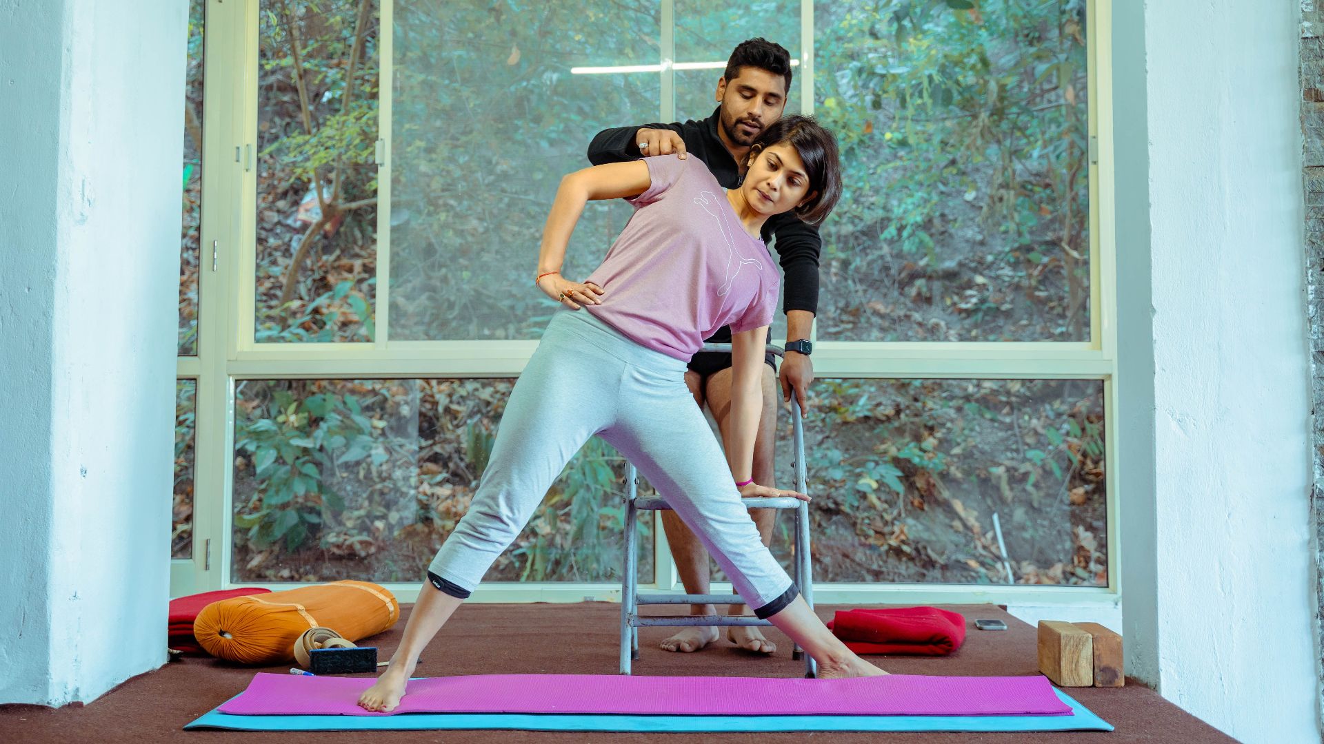 Yoga student stretching with instructor assistance in Rishikesh studio.