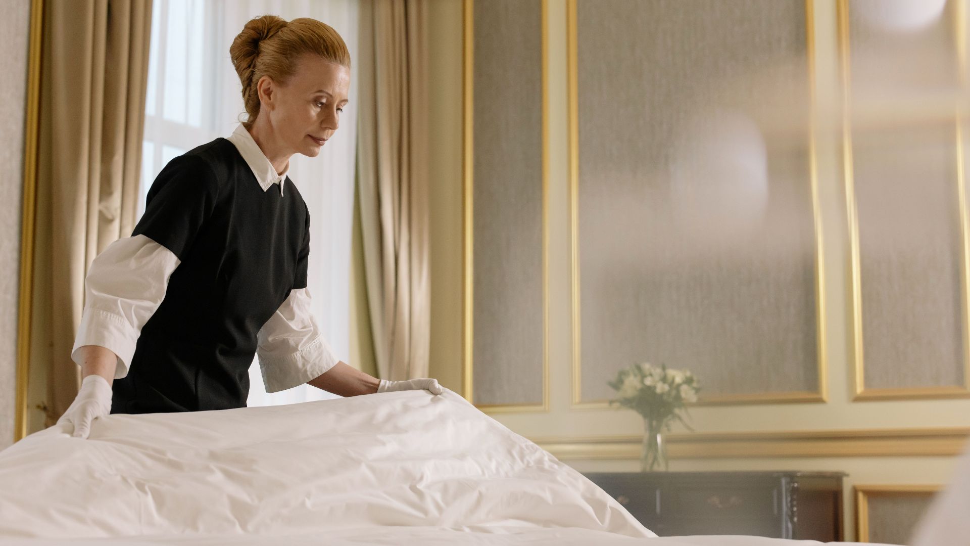 A professional housekeeper fixes a bed in a luxurious hotel room.