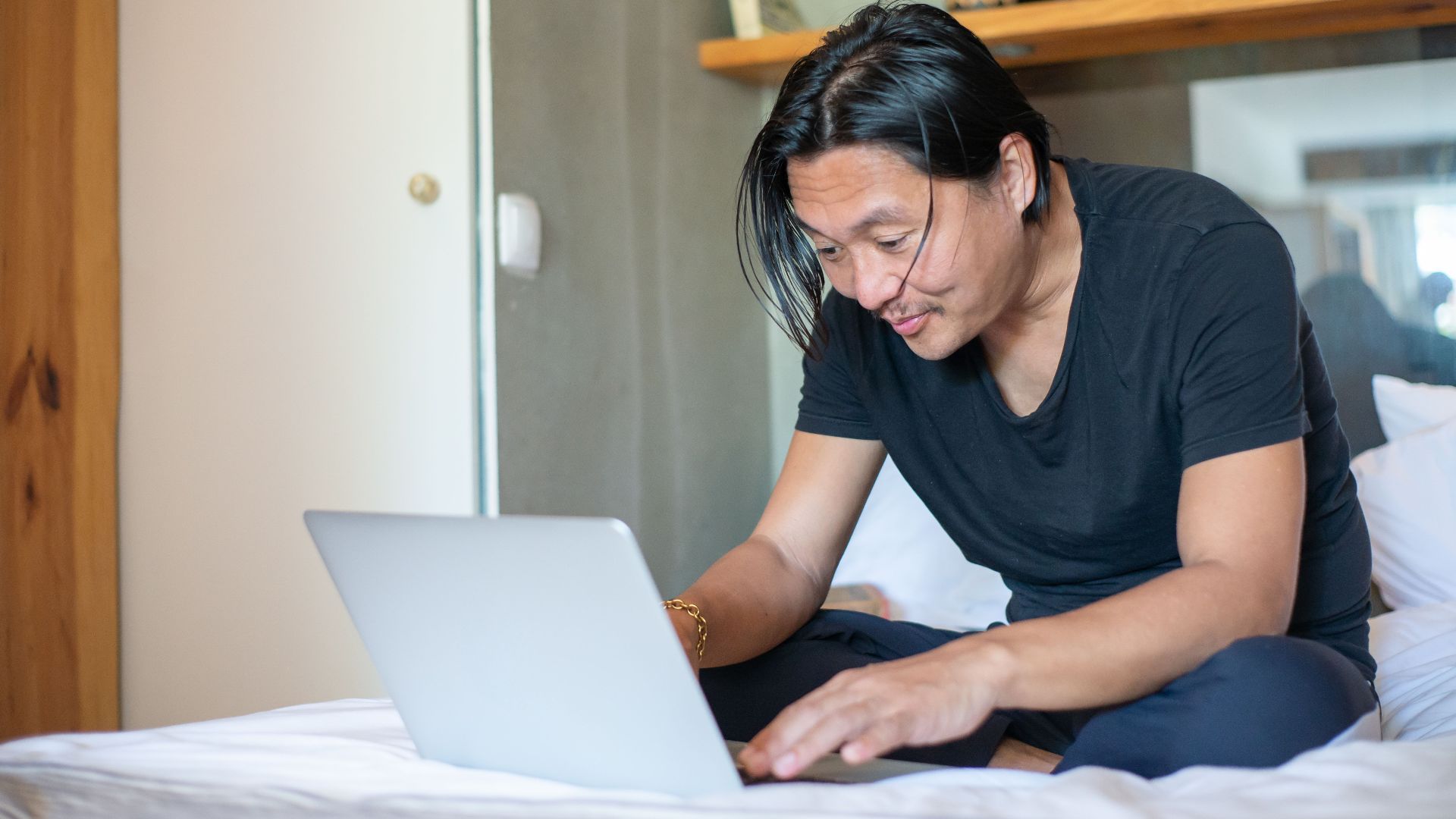 Man sits comfortably on his bed working remotely with a laptop, exemplifying modern freelance lifestyle.