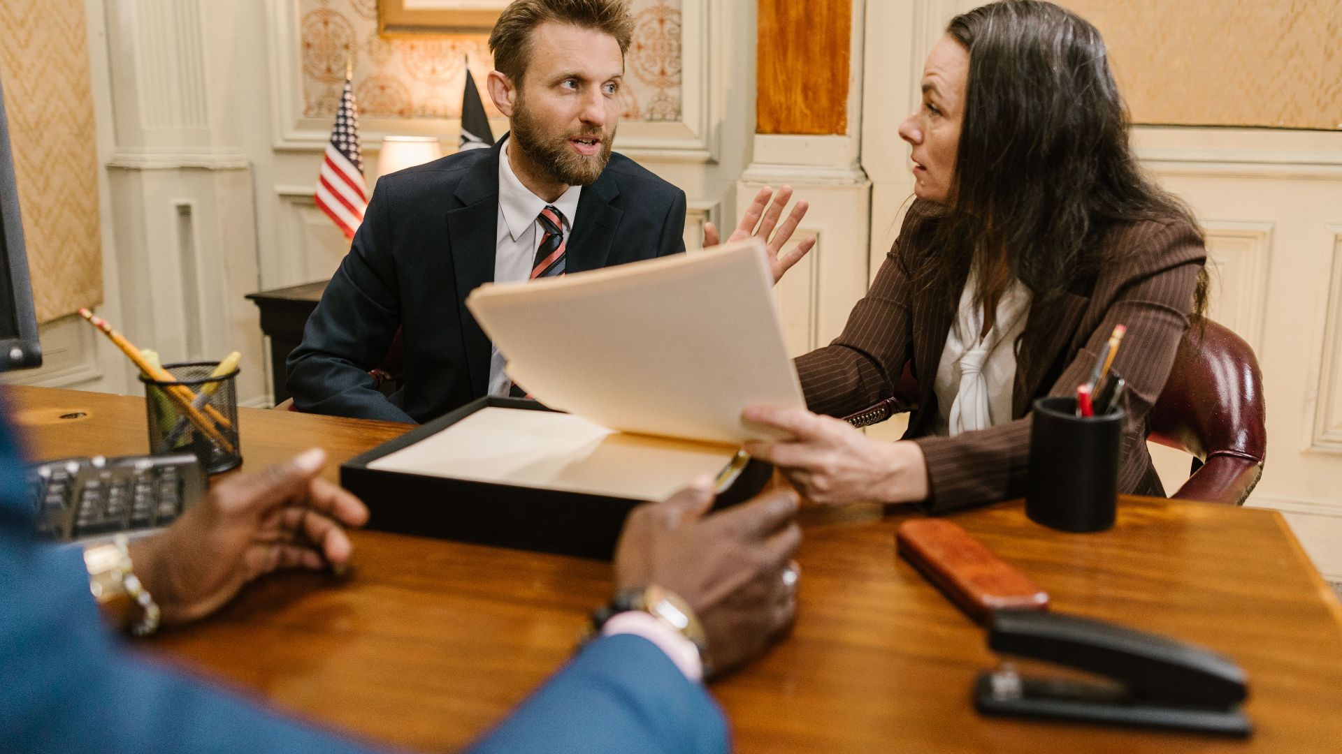 Diverse group in a corporate office engaged in a formal meeting. Professional attire and documents suggest a business discussion.