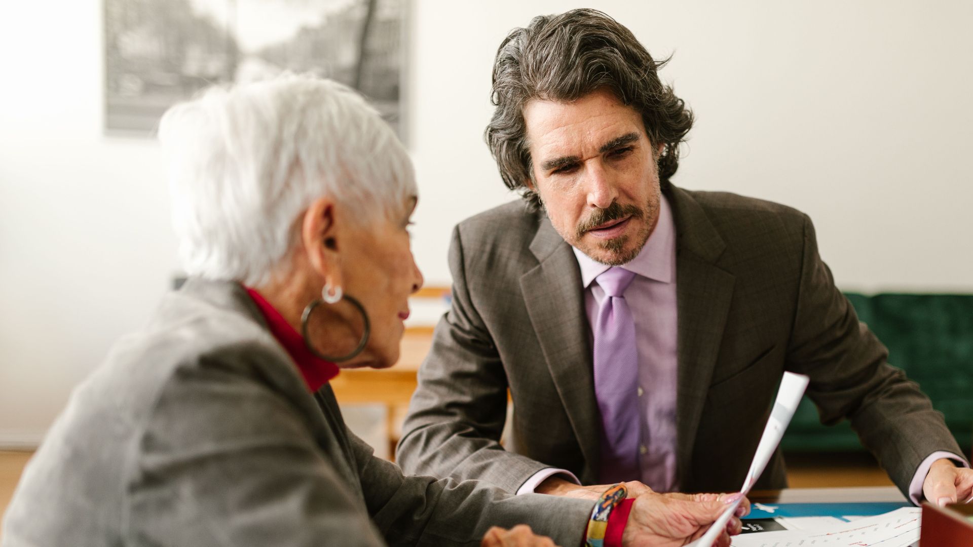 Elderly business professionals discussing reports in a modern office setting.