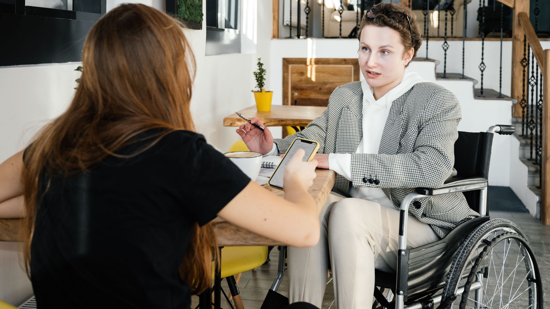 Concentrated female using wheelchair talking to coworker during coffee break in modern cafeteria