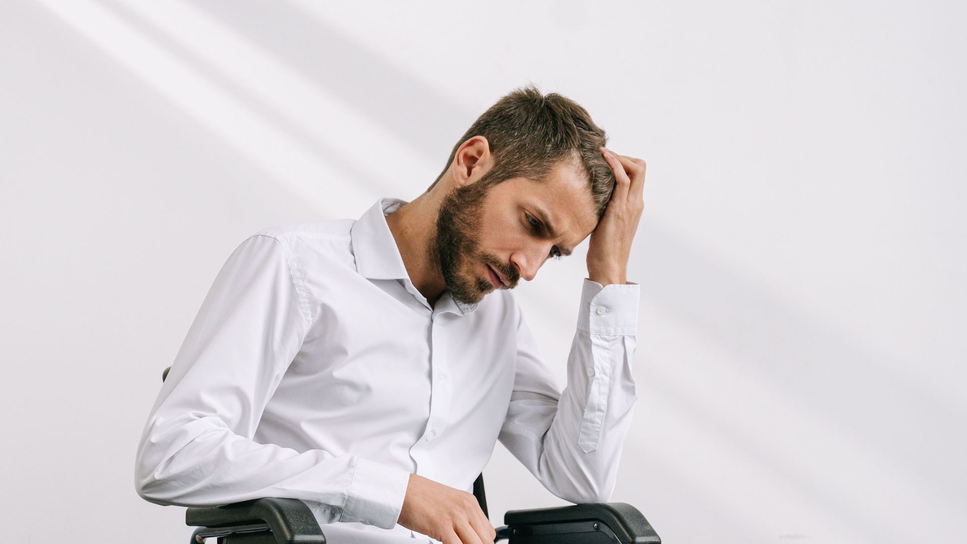 Adult man in a wheelchair using a laptop indoors, appearing thoughtful and focused.
