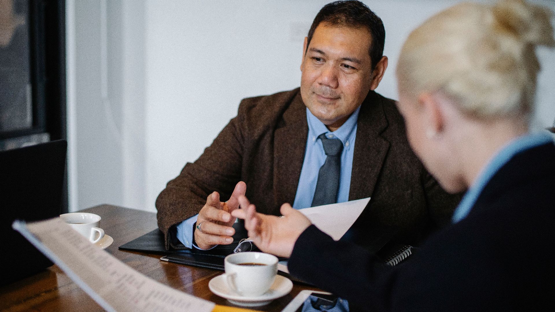 Professional diverse employees sitting at table with documents and cup of coffee and talking during work on new business project