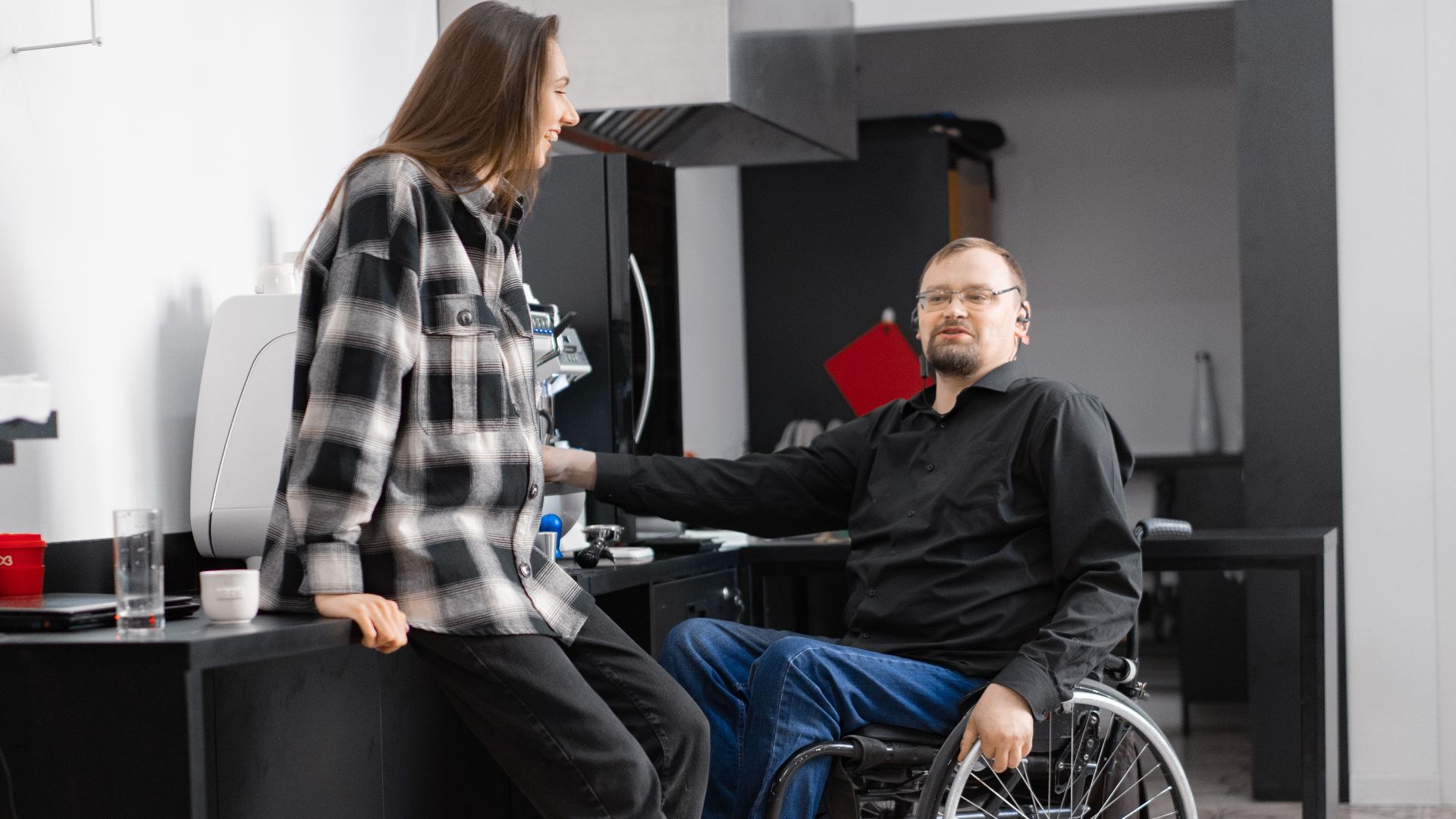 A man in a wheelchair and a woman conversing in a sleek, modern kitchen.