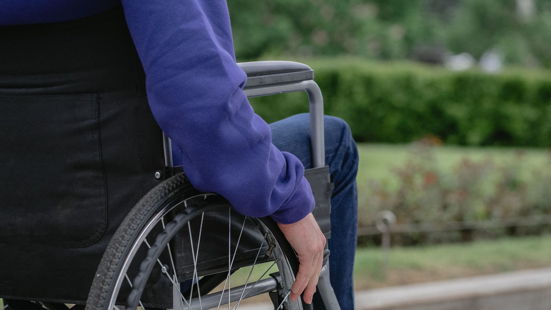 Individual in a wheelchair on a paved walkway outdoors, showcasing mobility and independence.