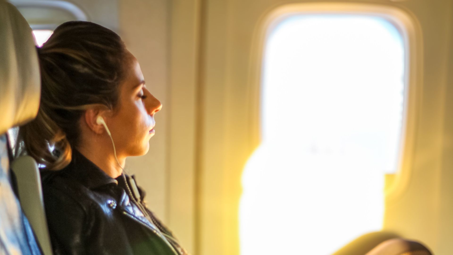 A woman enjoys a tranquil moment on a flight, gazing out the window with headphones on.