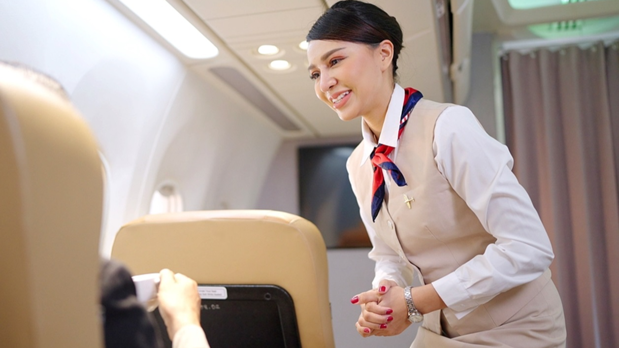 Friendly Asian female flight attendant serving food drink and talking to passengers on airplane.