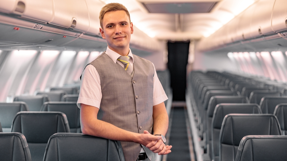 Male flight attendant in uniform standing in an empty aircraft passenger salon