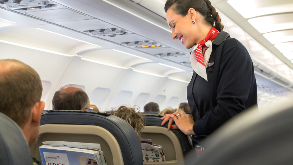 A female flight attendant in uniform is speaking with a passenger