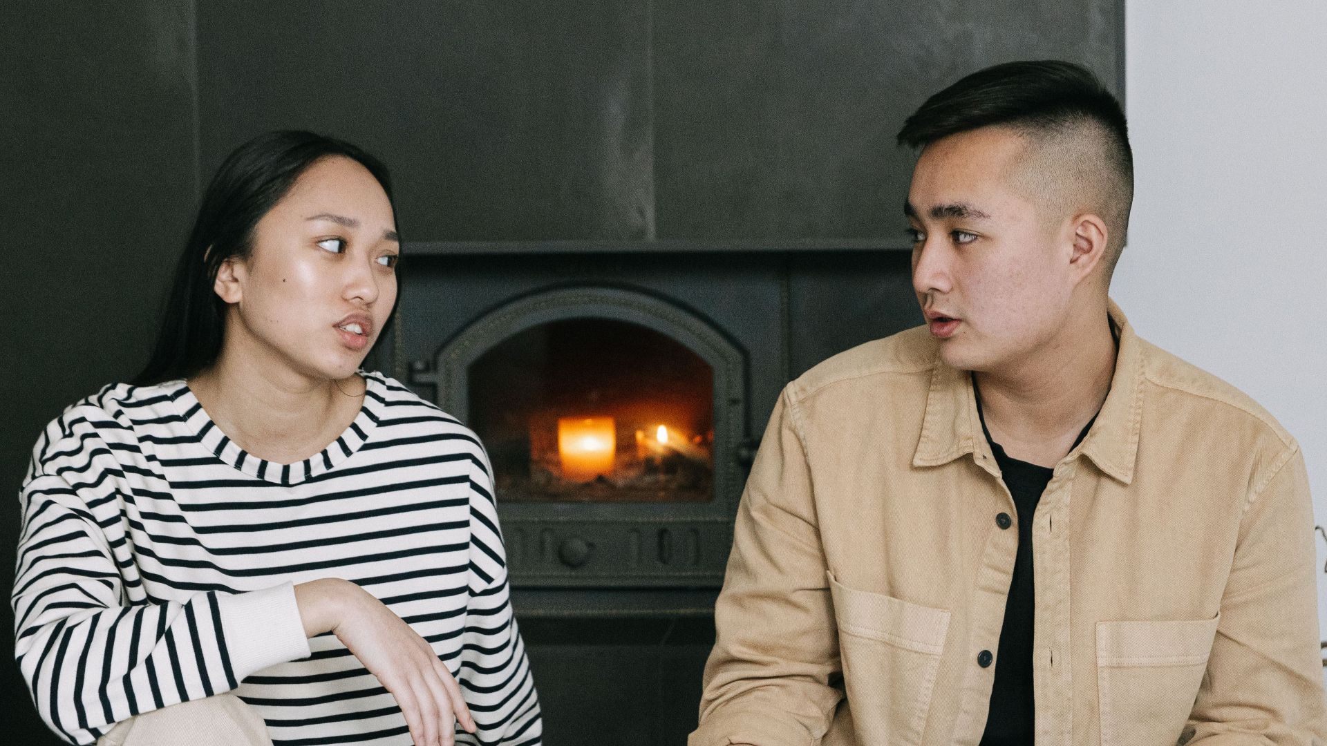 Young adults enjoy a casual conversation by the fireplace in a modern, cozy living room.