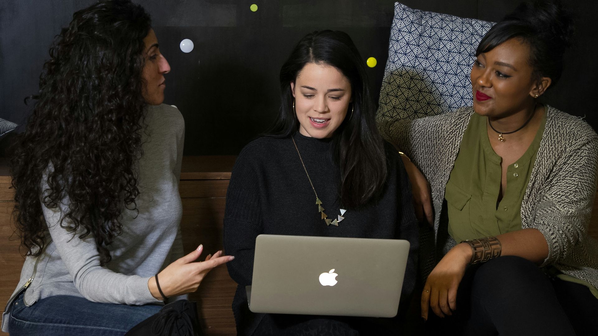 three women sitting on a bench looking at a laptop