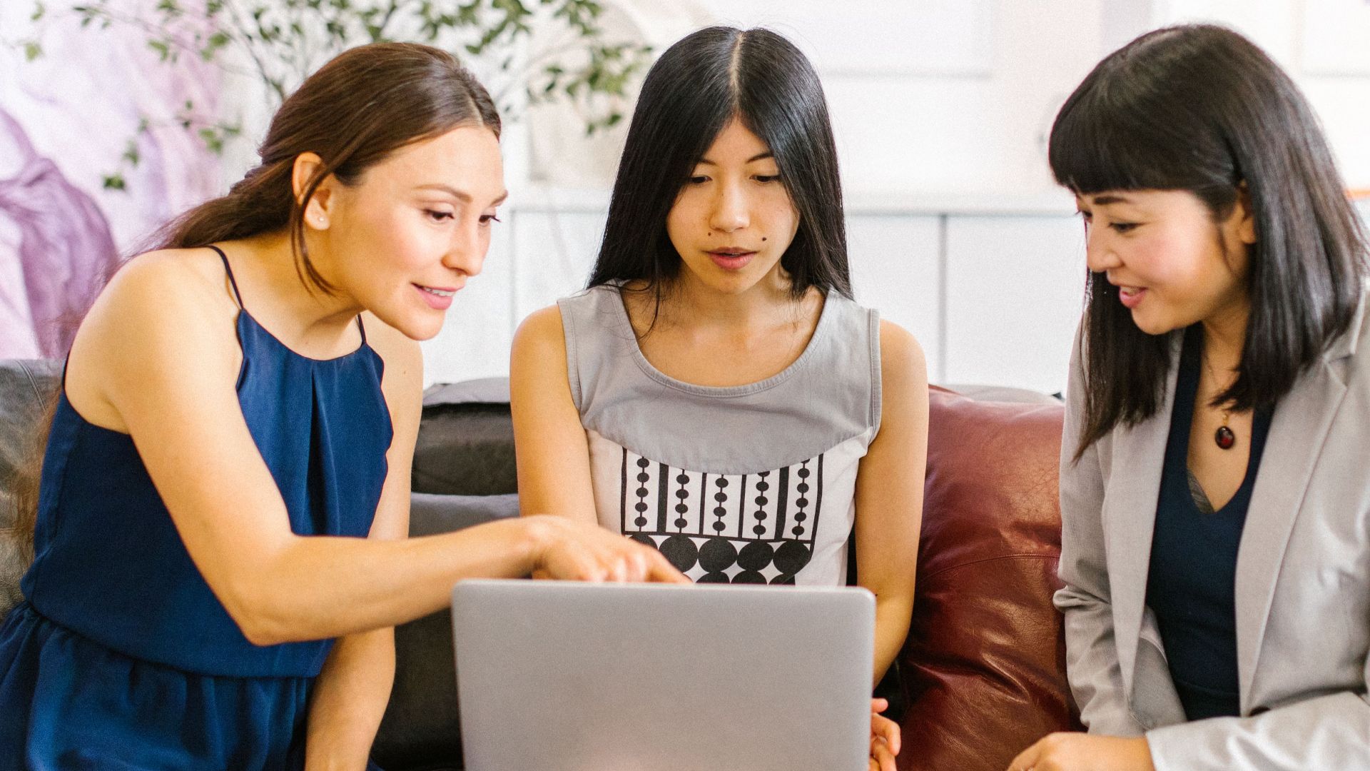 Three businesswomen collaborating on a laptop in a stylish, modern office.