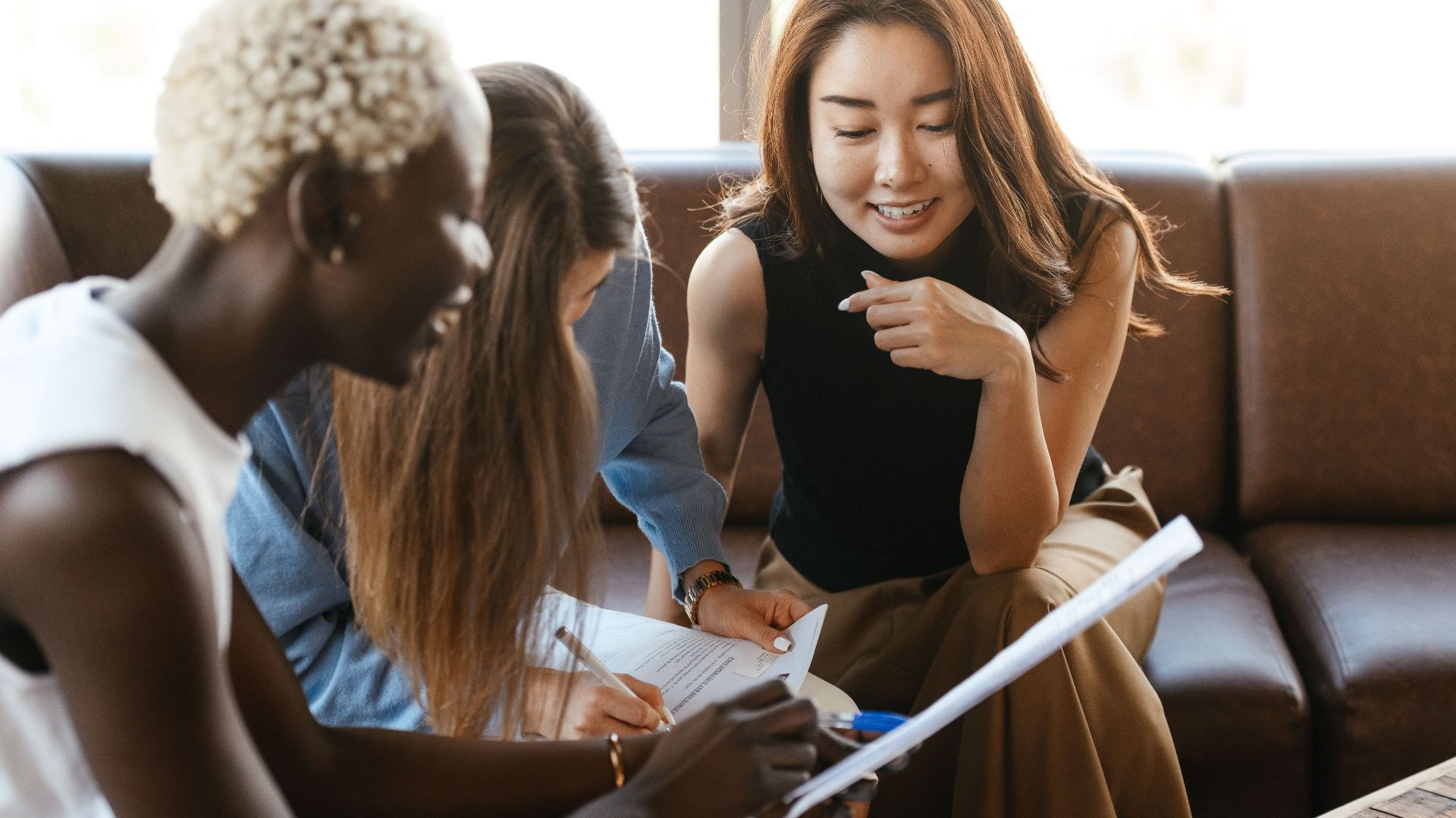 Young diverse happy business partners discussing contract and checking document in office in daytime