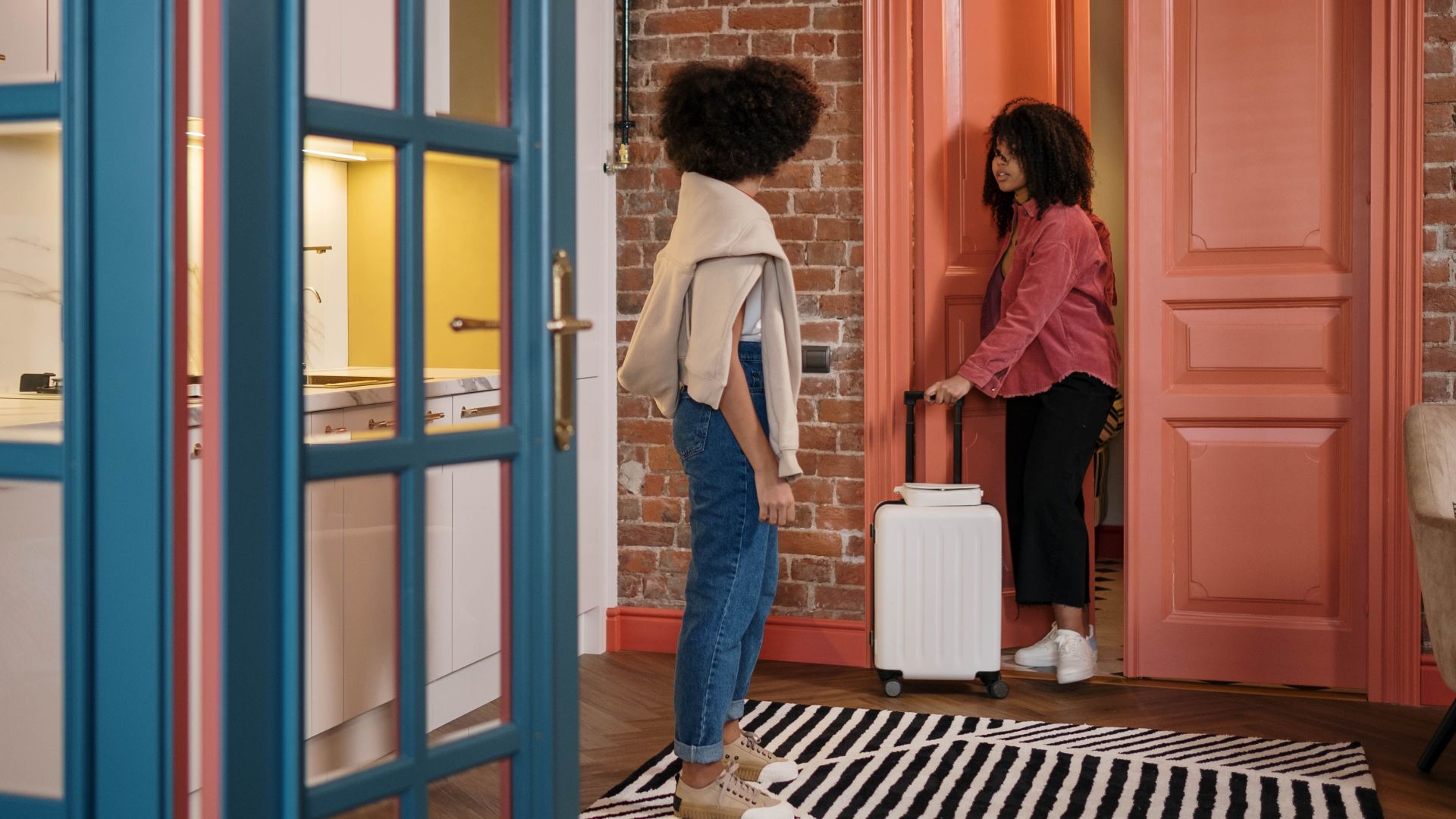 Two women with luggage in a stylish apartment hallway, getting ready to travel.