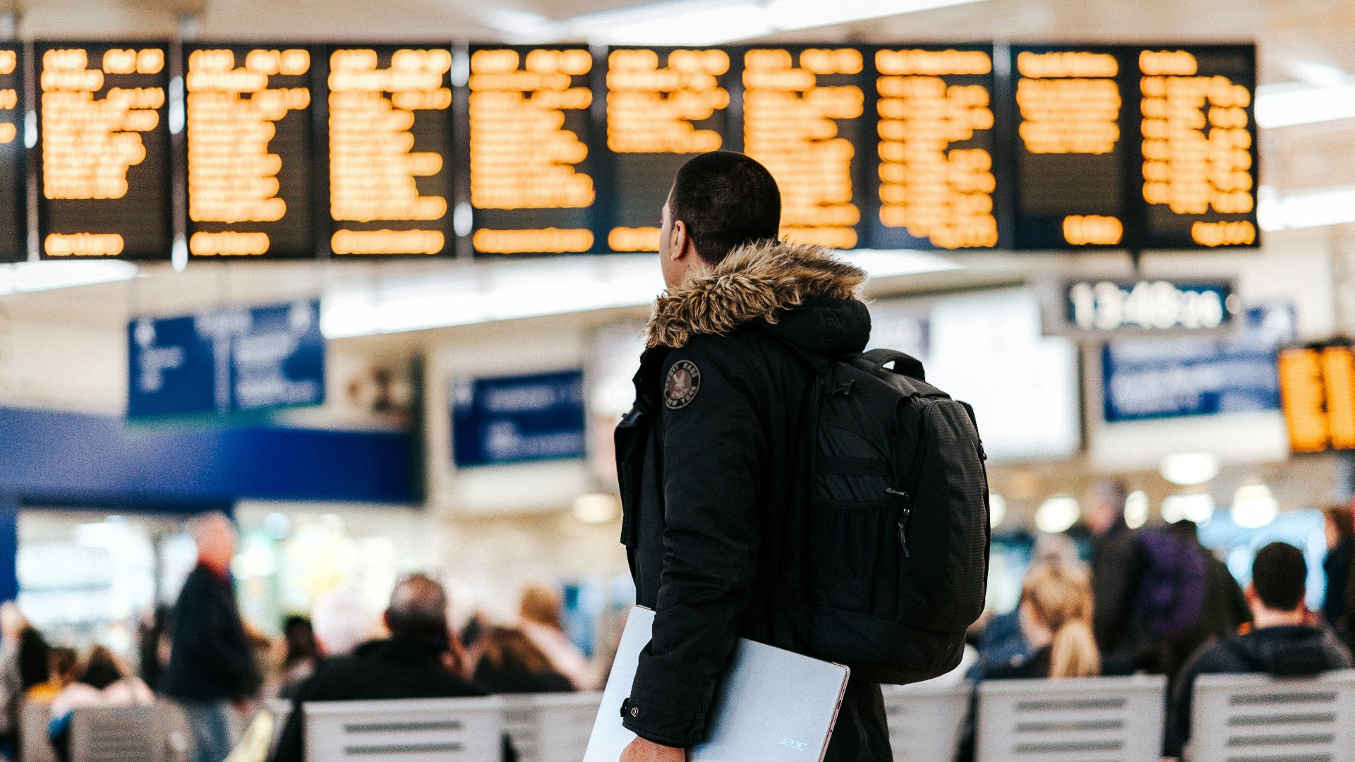 man standing inside airport looking at LED flight schedule bulletin board