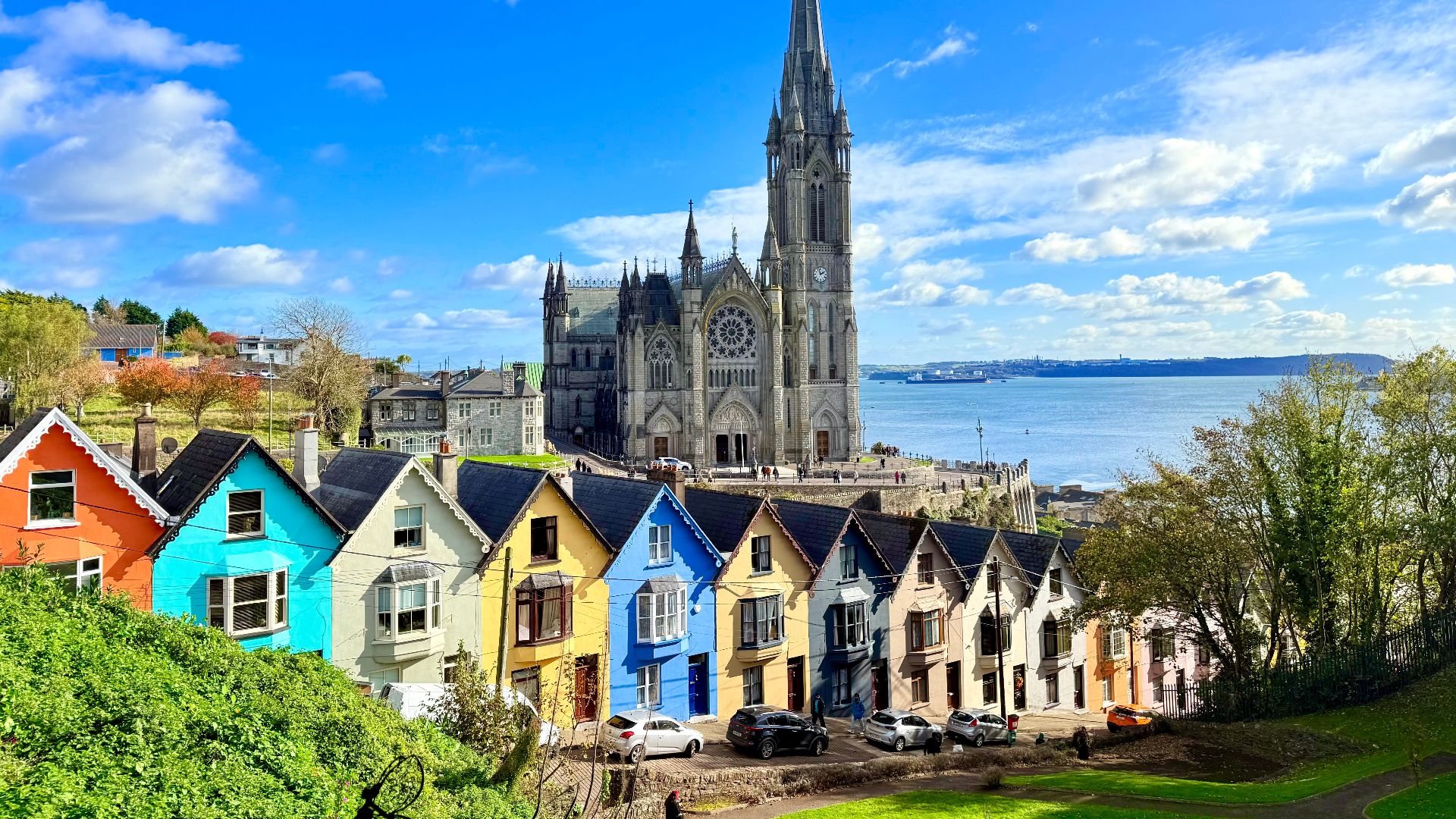 Vibrant colorful houses and cathedral in Cobh, Ireland with Atlantic Ocean backdrop.