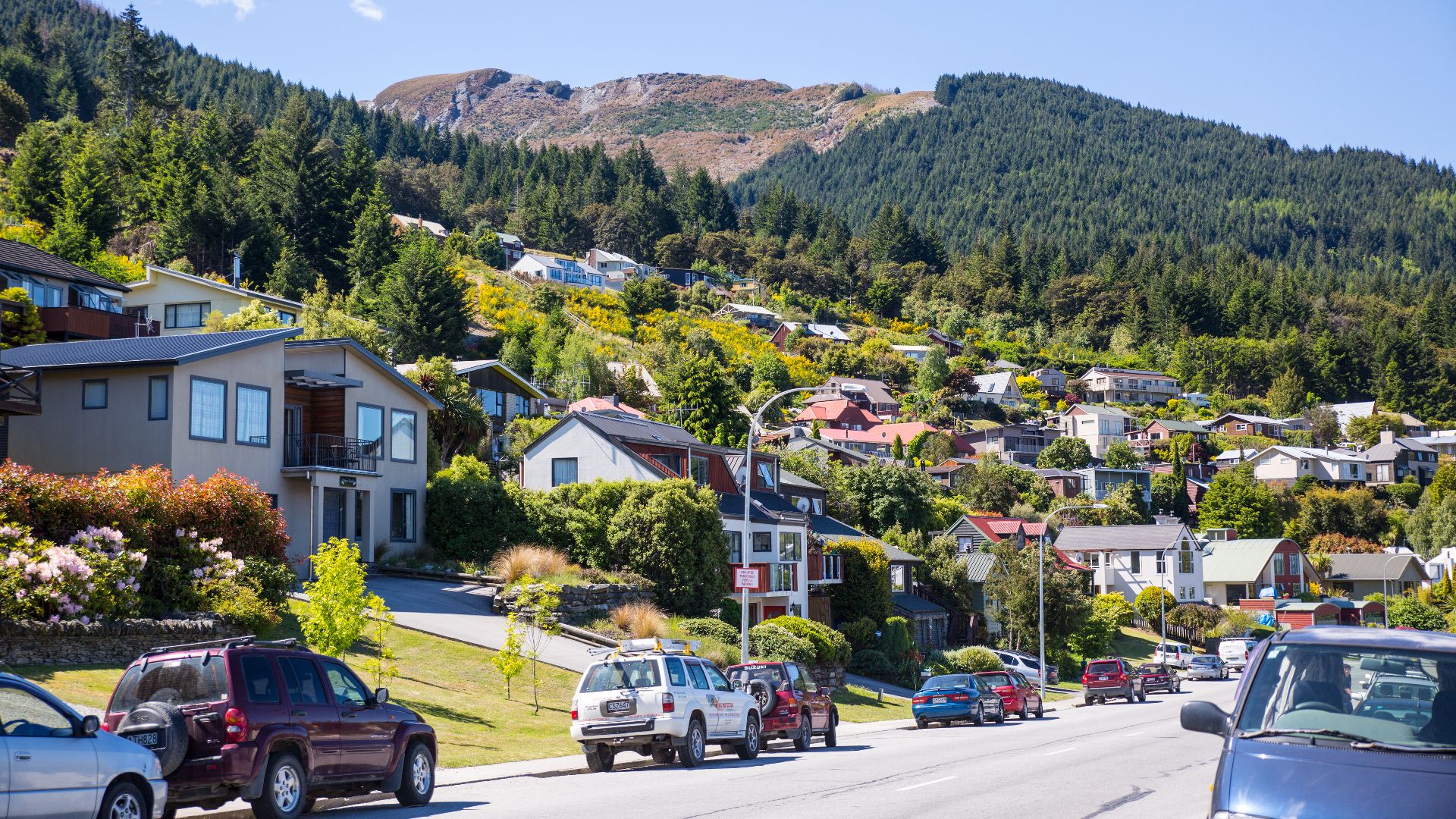 Vibrant suburban street in Queenstown, New Zealand, nestled against lush mountains.