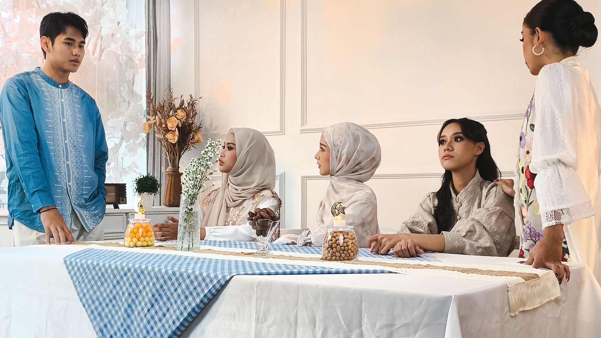 A family in traditional attire gathers indoors for a meal.