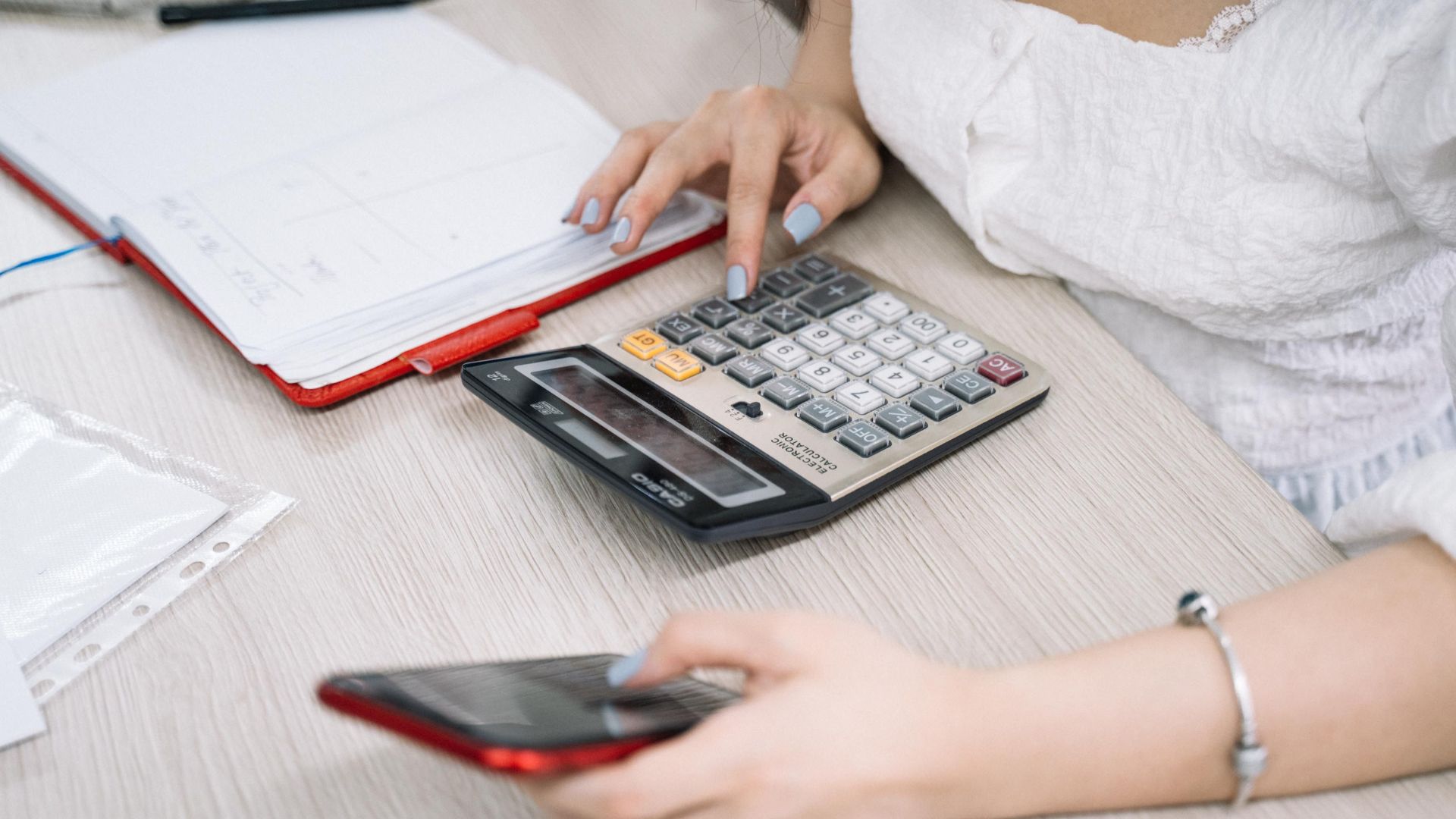 Close-up of a woman using a calculator and phone at her office desk.