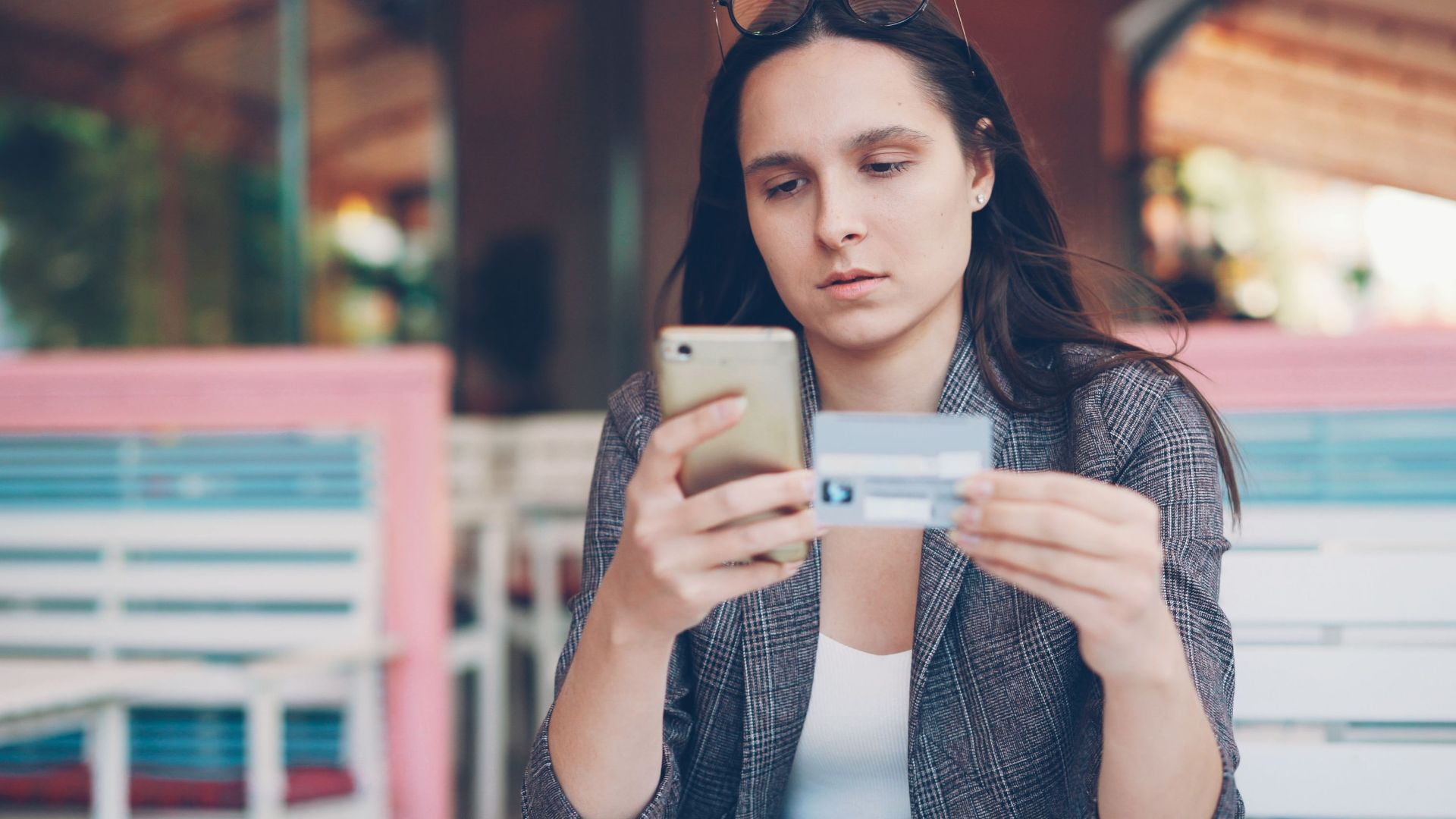 Woman using smartphone for online shopping at a cafe with credit card in hand.