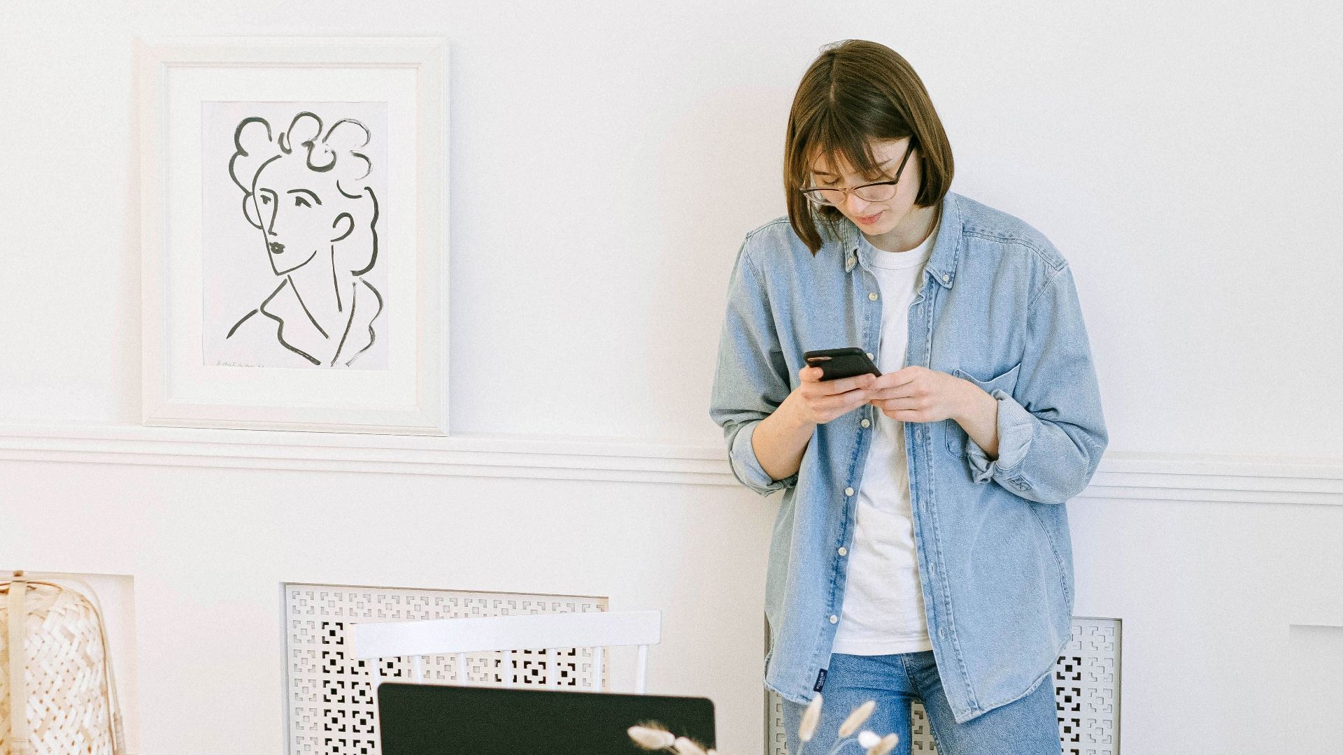 Woman in casual attire texting and working in a modern home office setting.