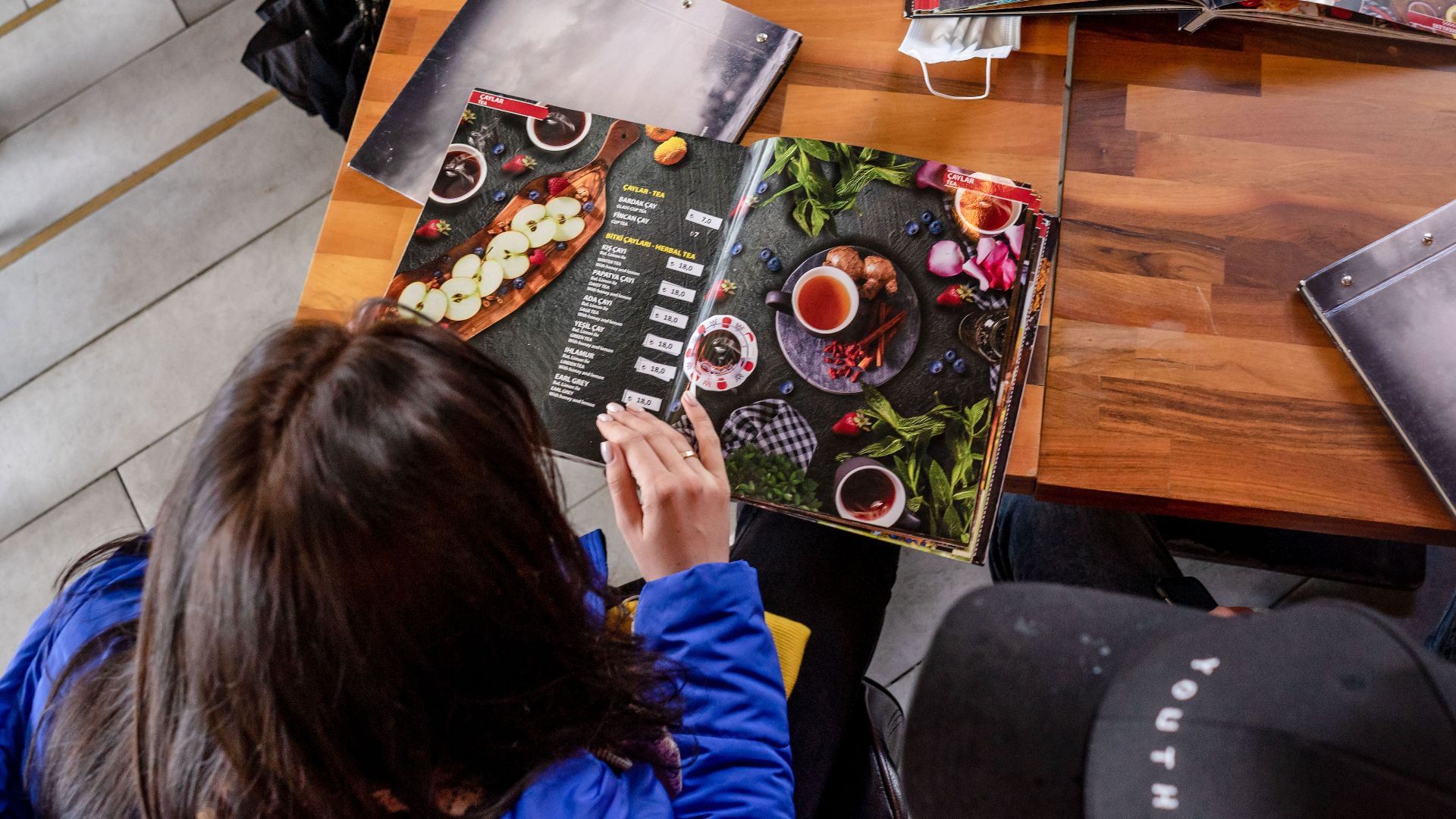 Two individuals explore food menus at a wooden table in a cozy café.