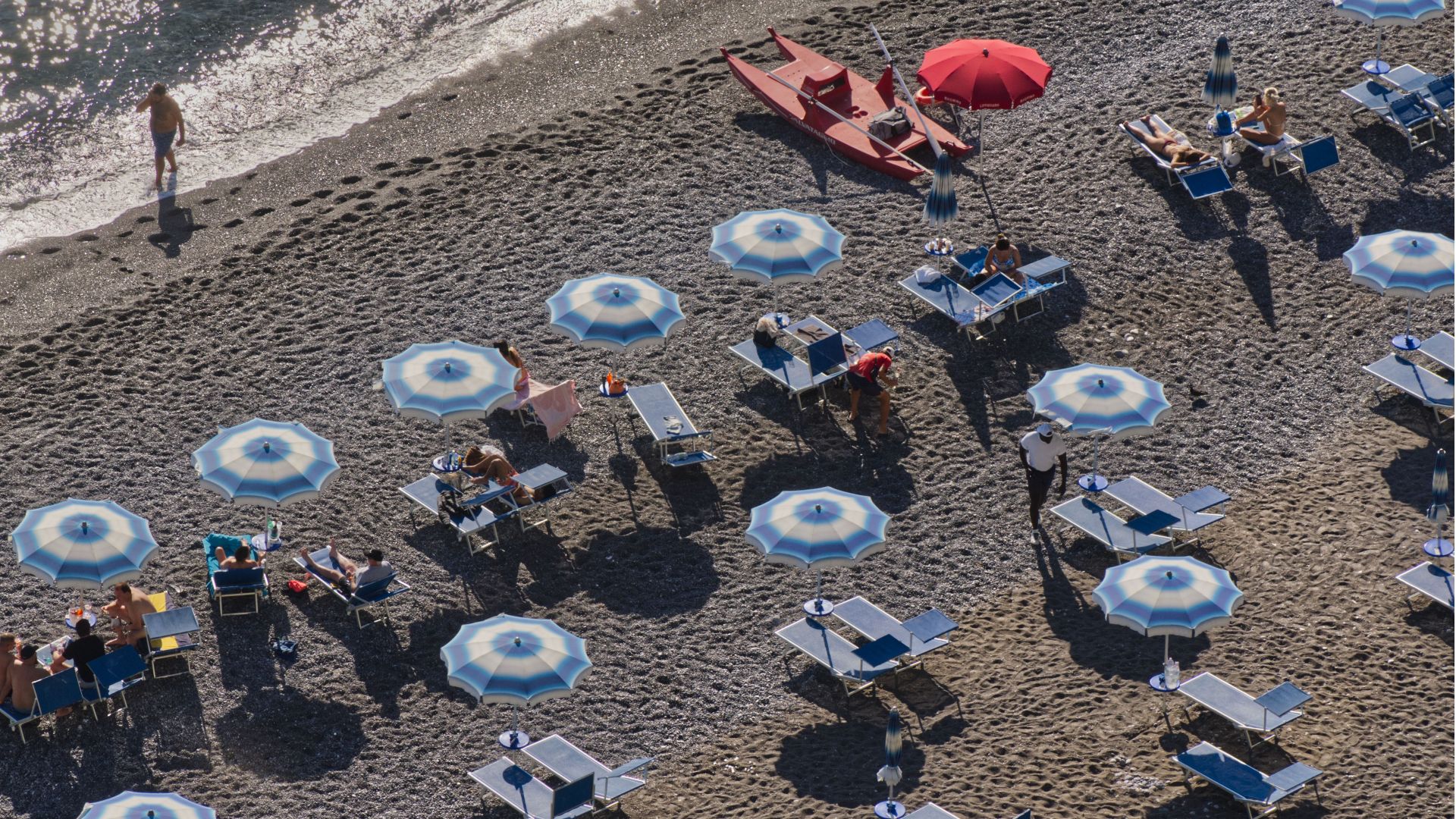 Aerial shot of people relaxing on a beach with umbrellas and kayaks.