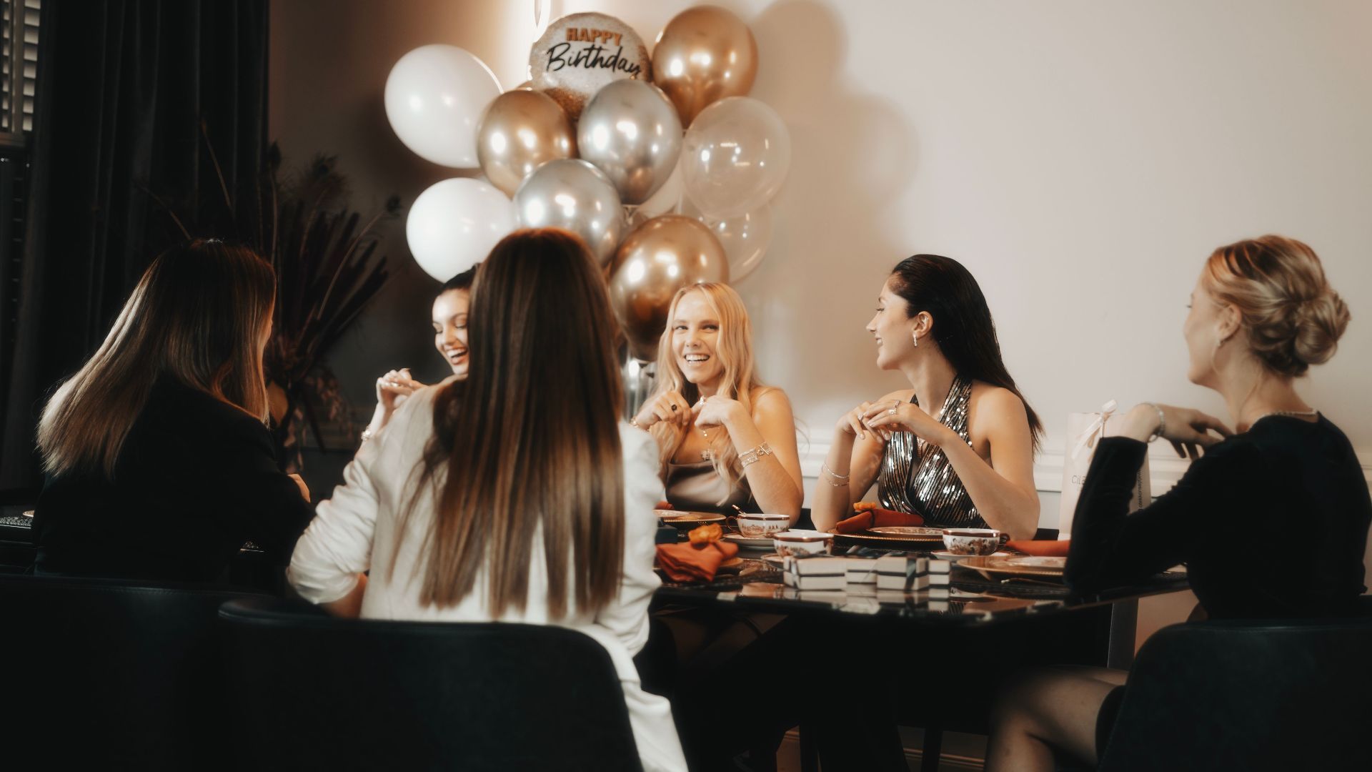 Group of women enjoying a birthday party with balloons inside. Lively and warm atmosphere.