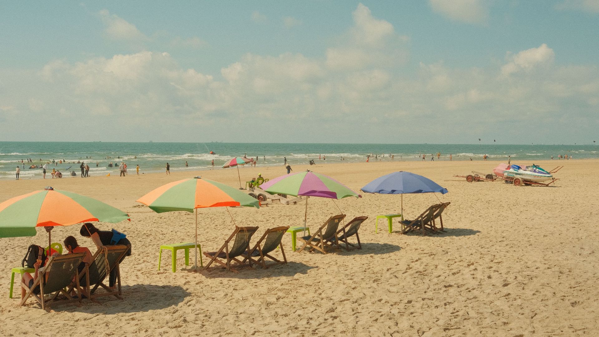 Scenic beach with colorful umbrellas, chairs, and people enjoying a sunny day.