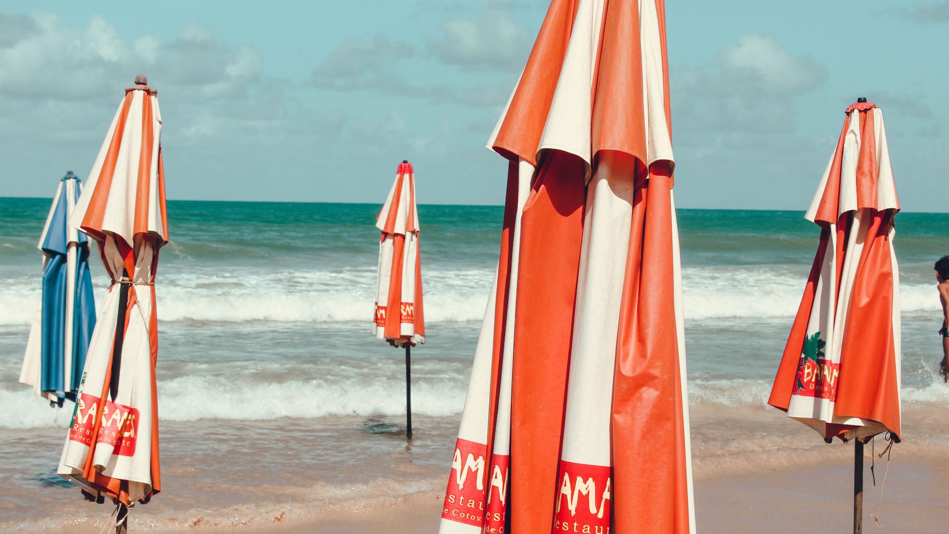 Brightly colored striped umbrellas stand on an empty beach, creating a vibrant coastal scene.