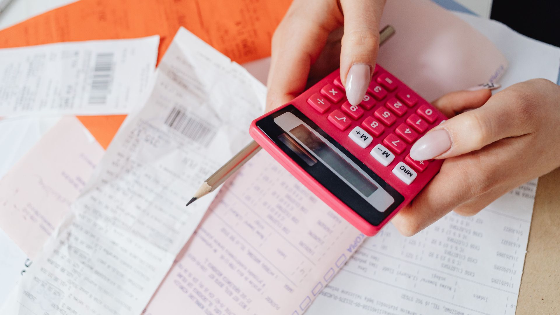 Hands using a pink calculator to manage expenses amidst various receipts and documents.