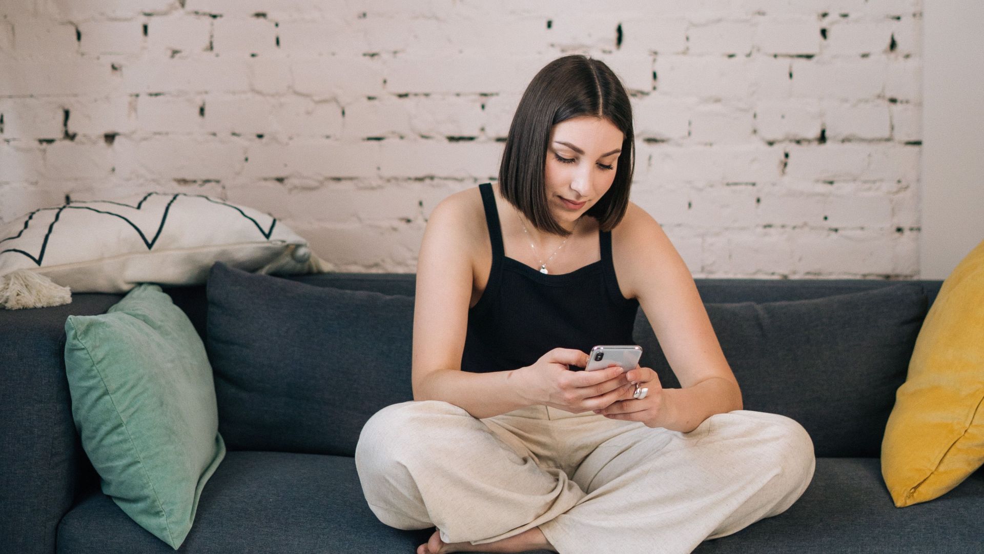 A young woman in casual attire sitting on a sofa using her phone in a modern living room.