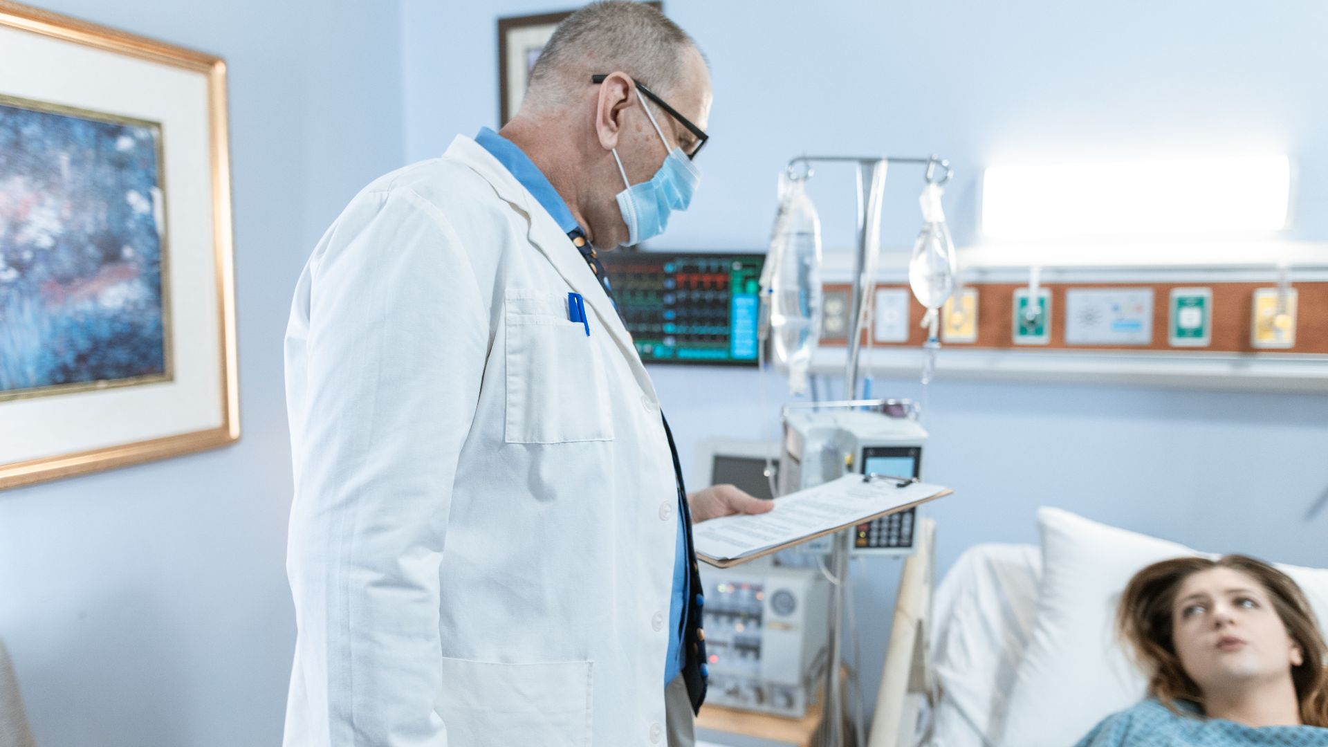 Doctor checks on patient in hospital room with medical equipment.