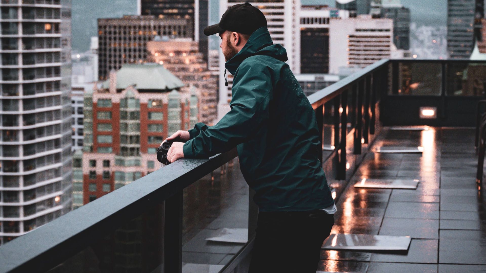 Man viewing cityscape from rooftop, modern urban setting with skyline in background.