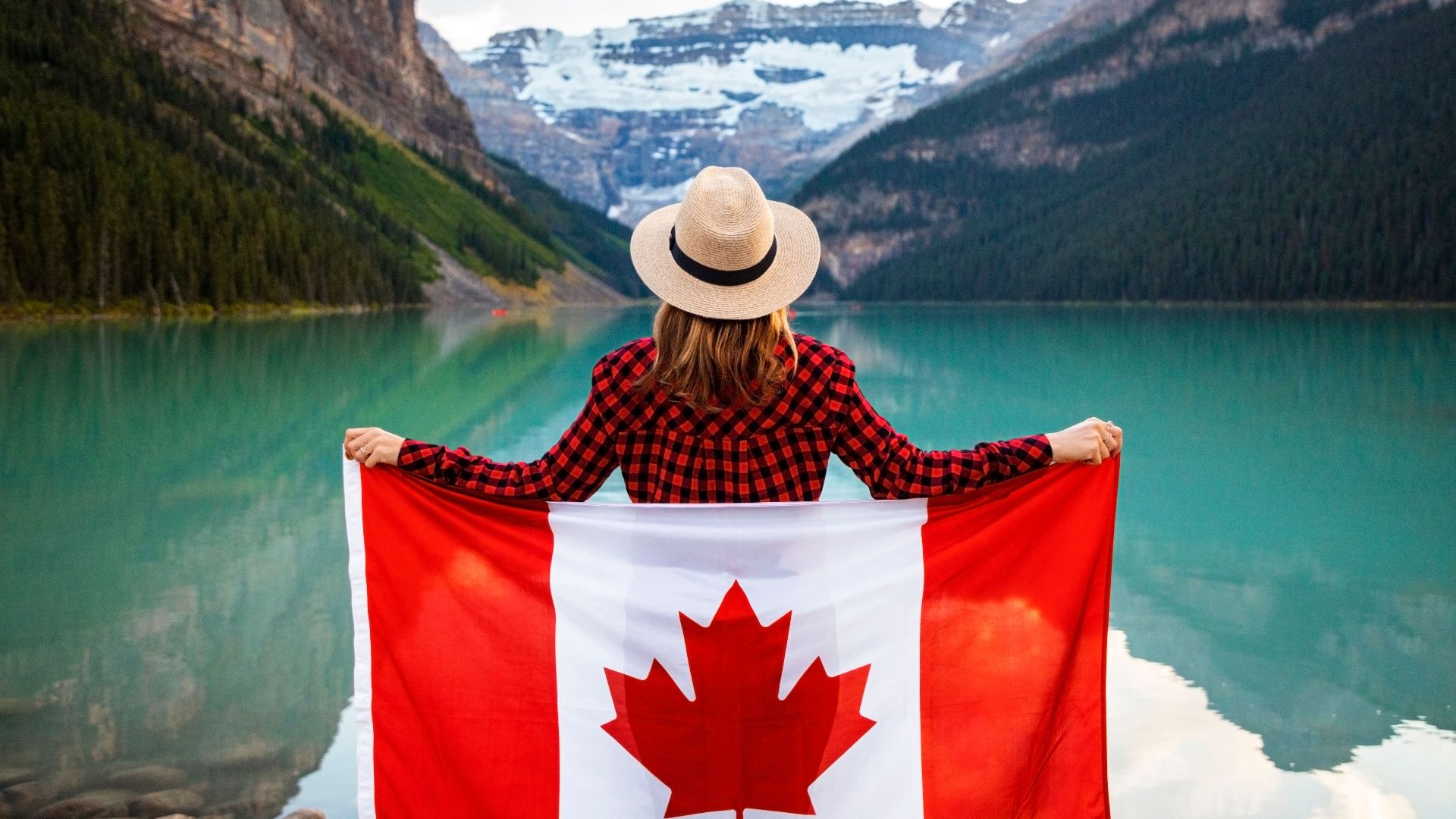 Woman holding a Canadian flag at stunning Lake Louise, Alberta, embracing nature and patriotism.