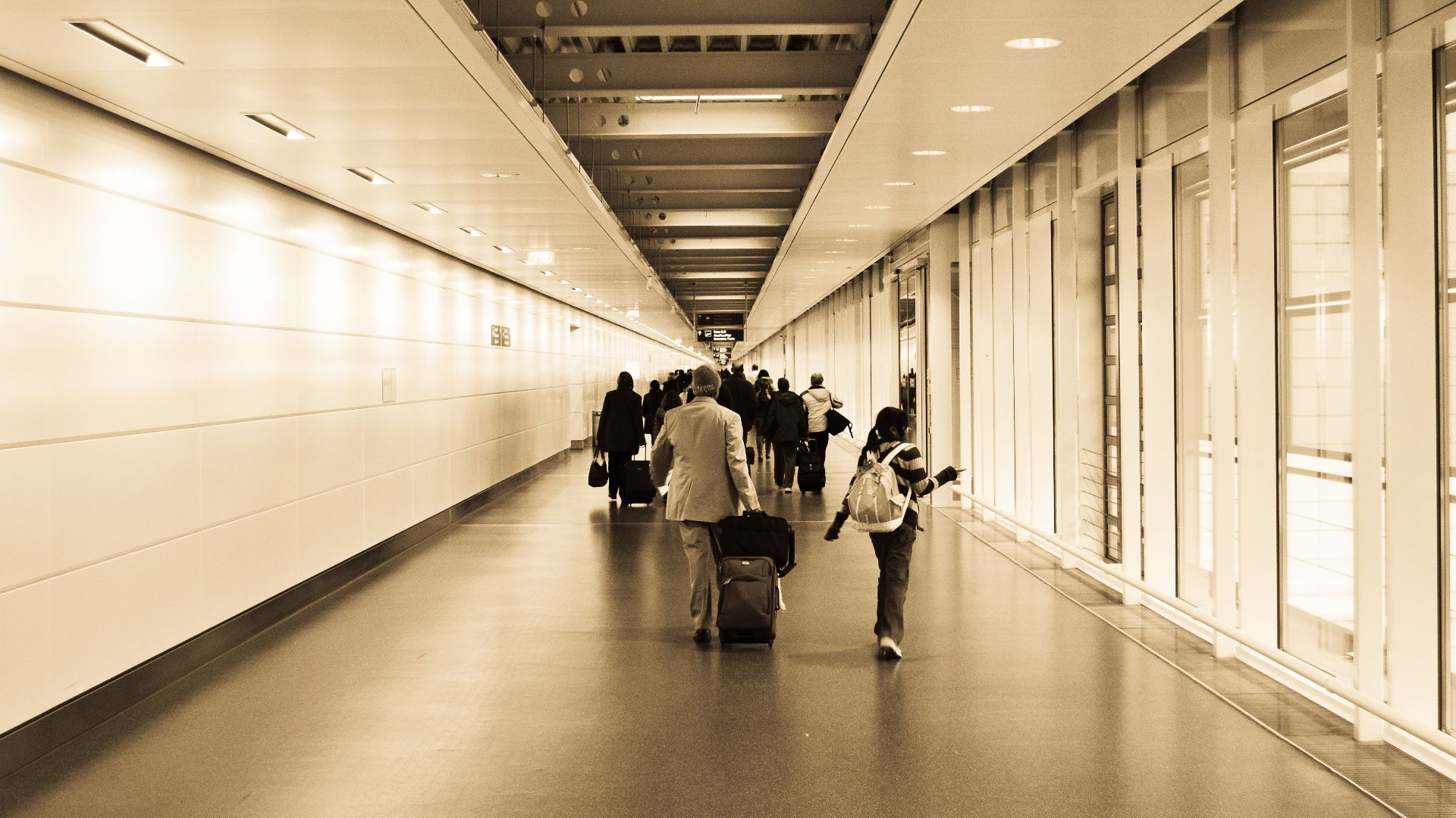 Travelers with luggage walking through a modern airport hallway with a vintage tone.