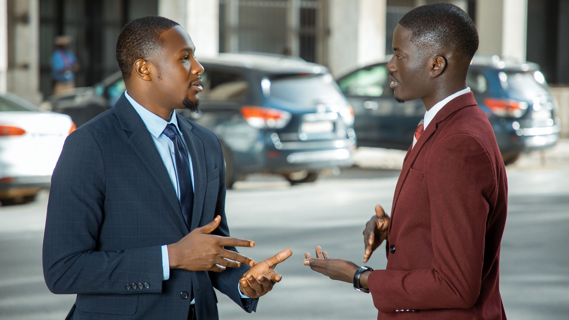 Two African businessmen in formal suits have a discussion on a city street in Dakar, Senegal.