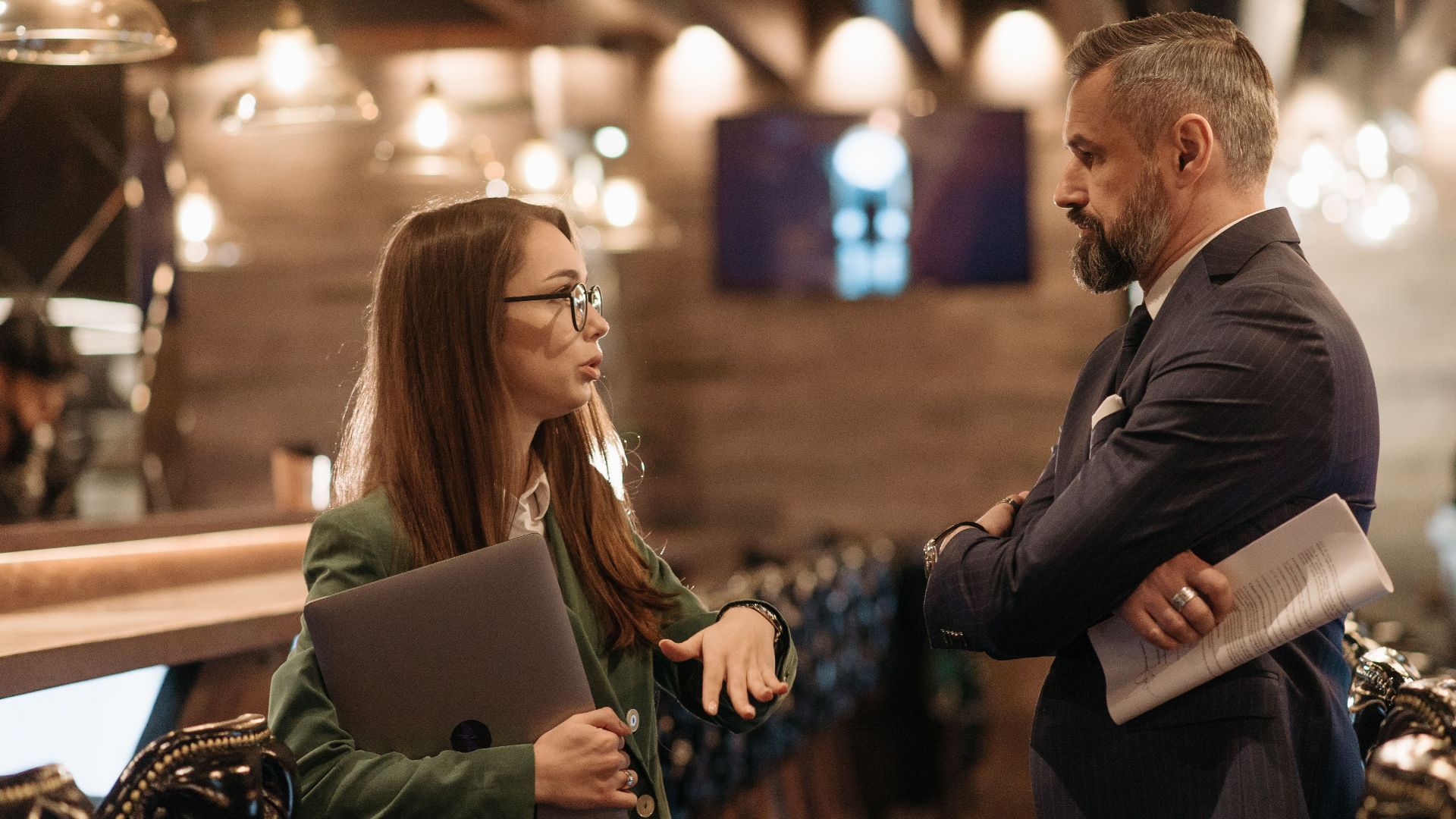 Two business professionals engaging in conversation in a stylish bar interior, highlighting modern work culture.