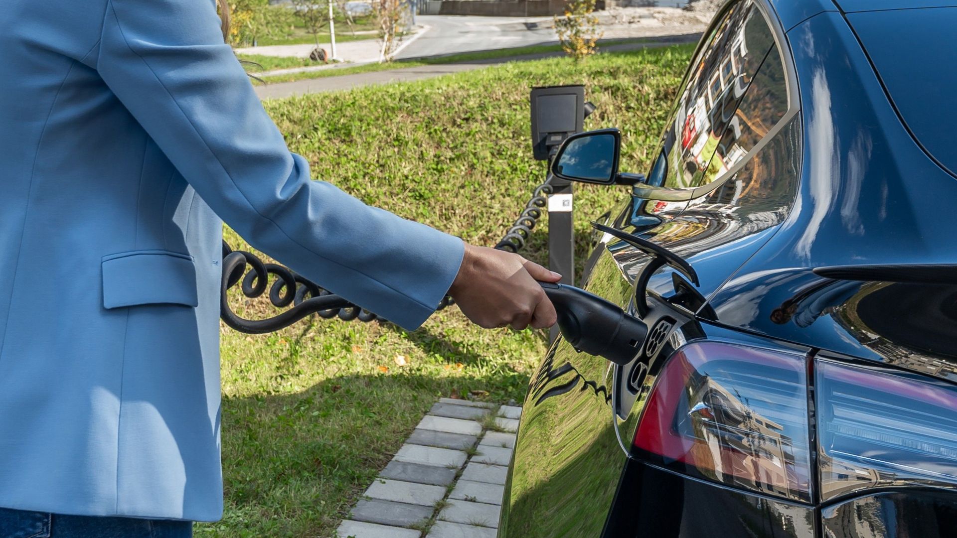 Person connecting an electric car to a charging station outdoors, showcasing green energy transition.