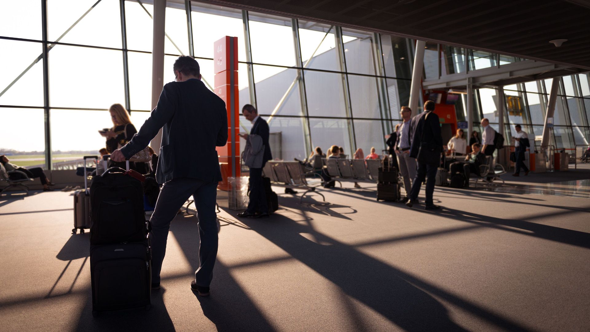 Travelers in a bustling airport terminal with carry-on luggage waiting for departure.