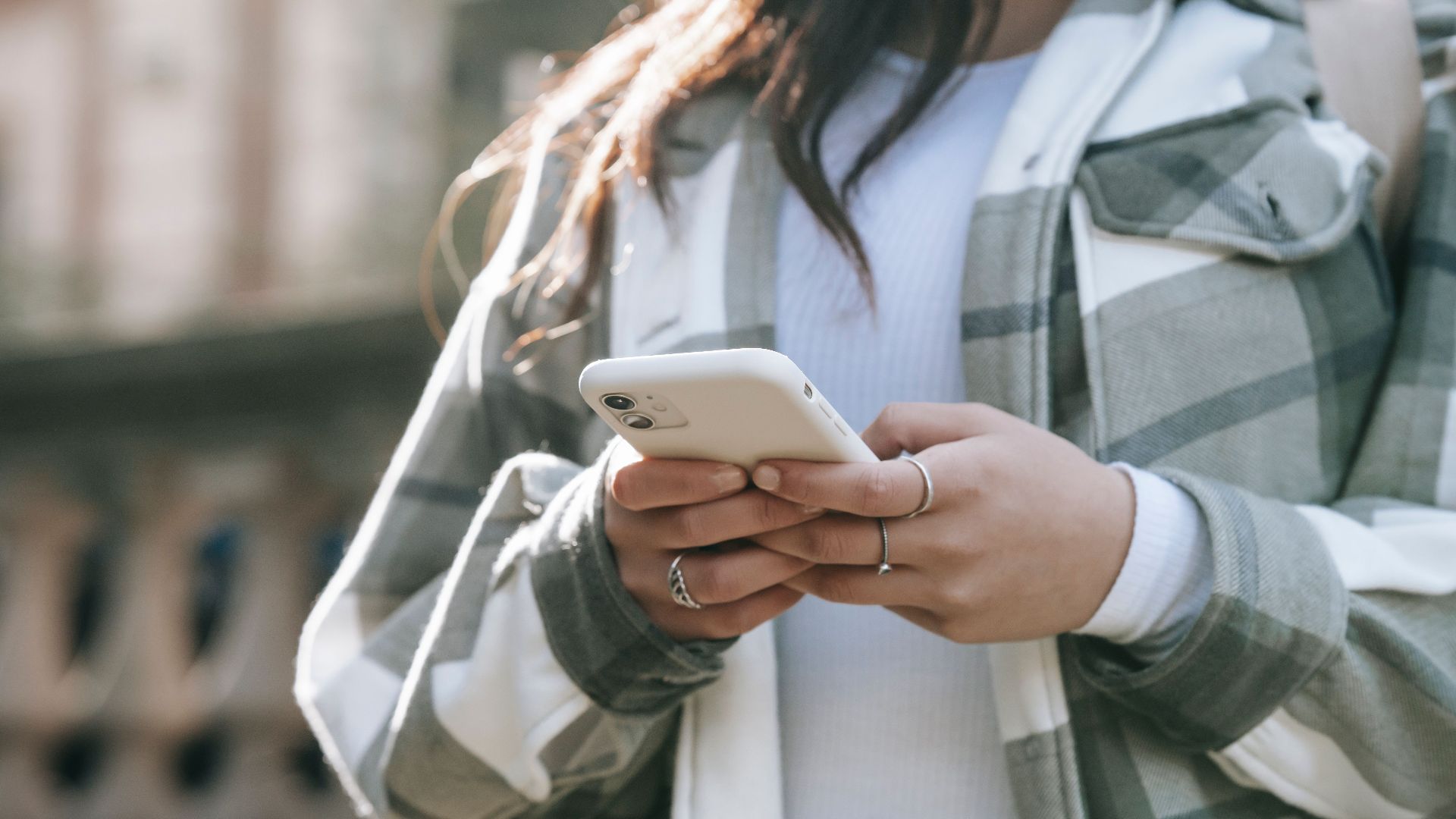Crop faceless young woman in casual outfit text messaging on phone in city street in daytime
