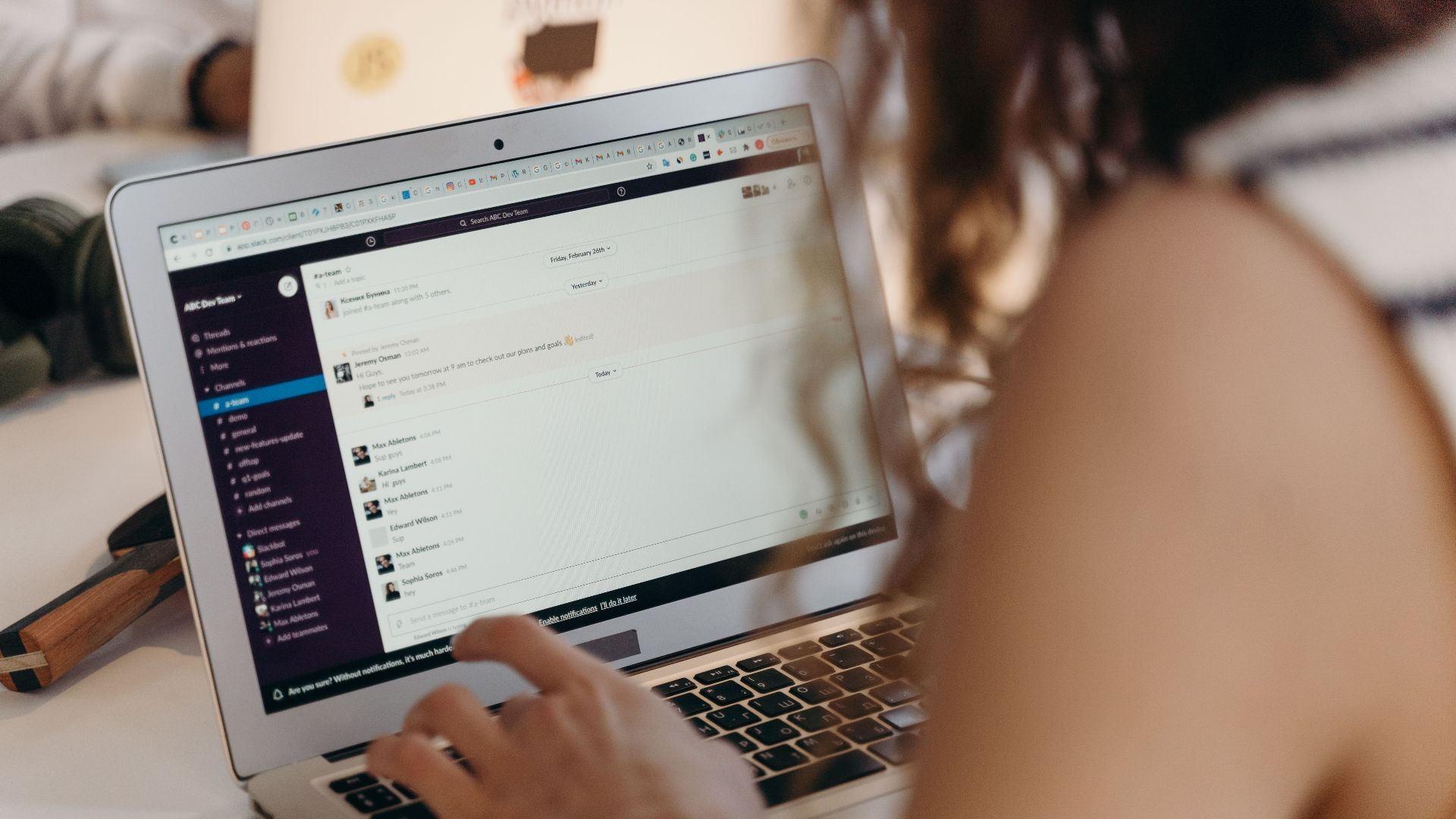 A businesswoman typing on a laptop in an office setting, using Slack for communication.