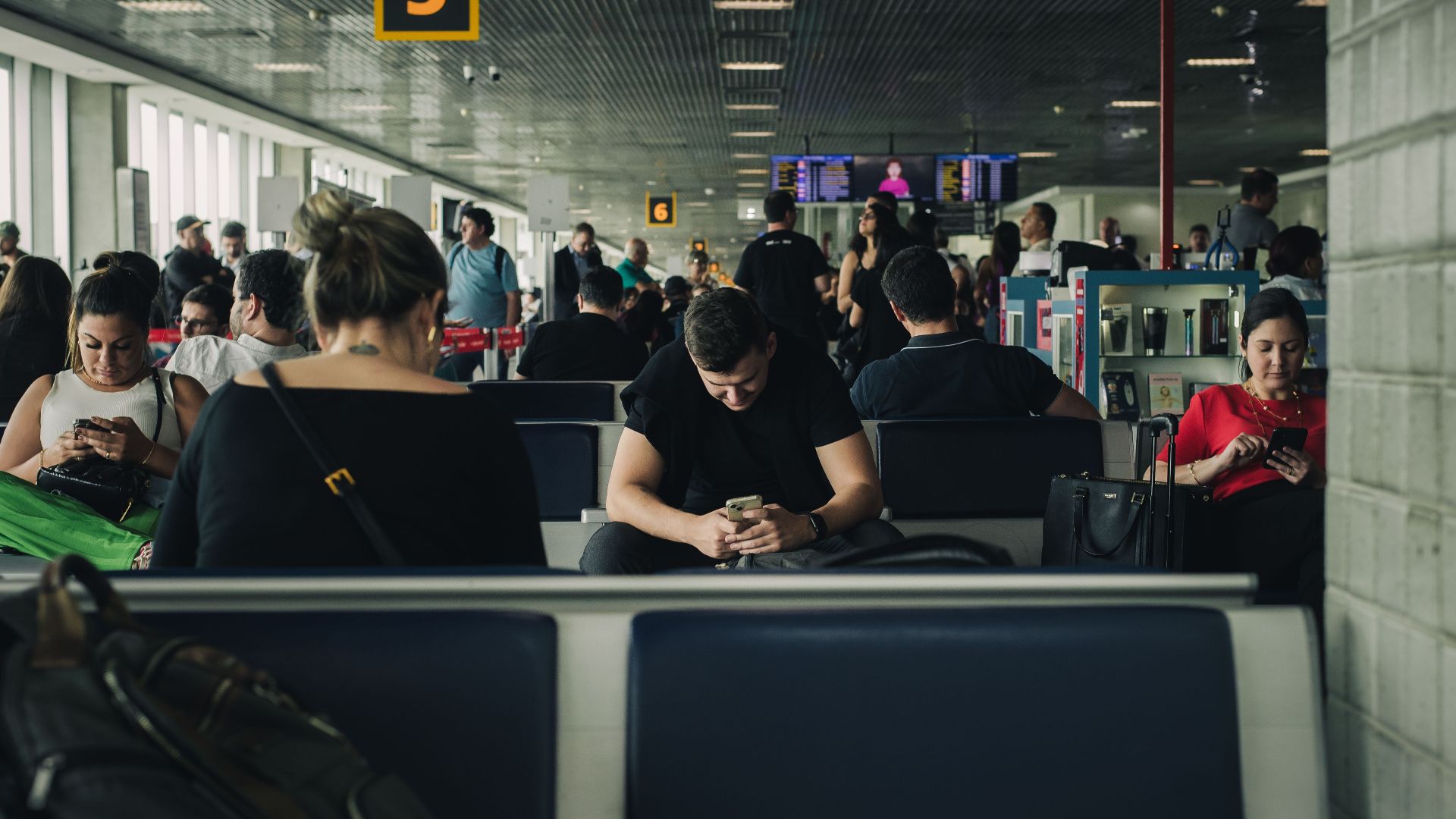 Travelers seated and waiting at São Paulo airport terminal, engaging with smartphones.