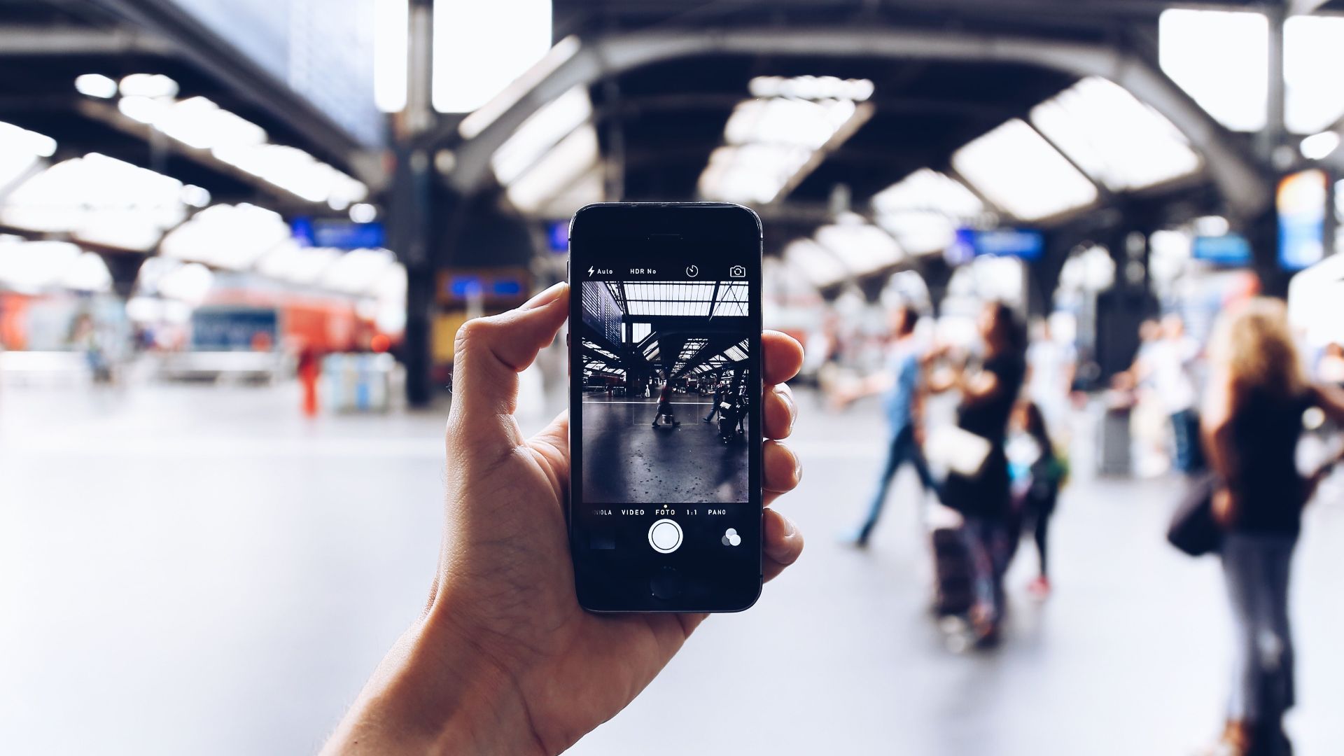 Hand holding a smartphone capturing the bustling atmosphere of a modern train station.